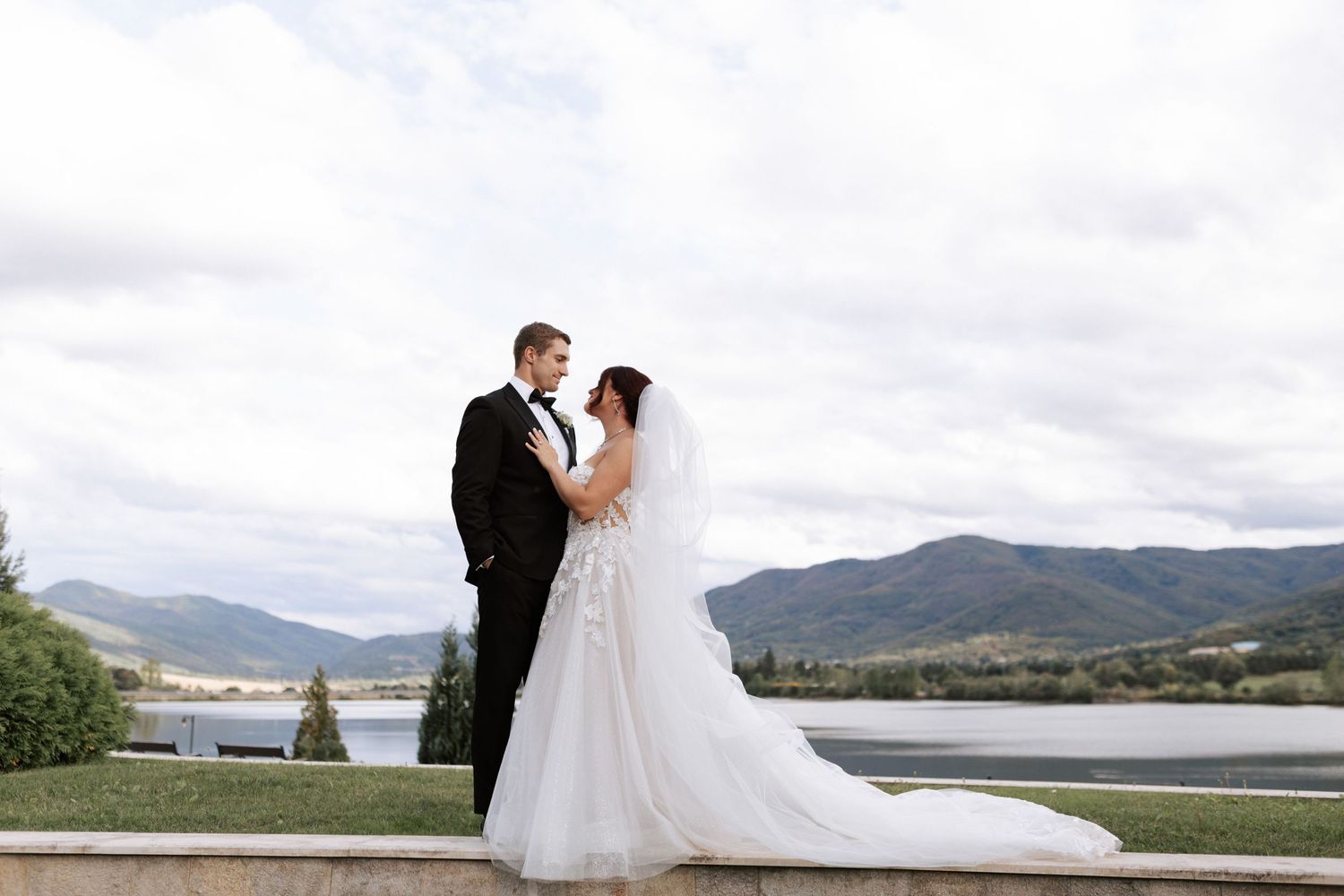 Wedding couple shares romantic moment with mountain lake backdrop.