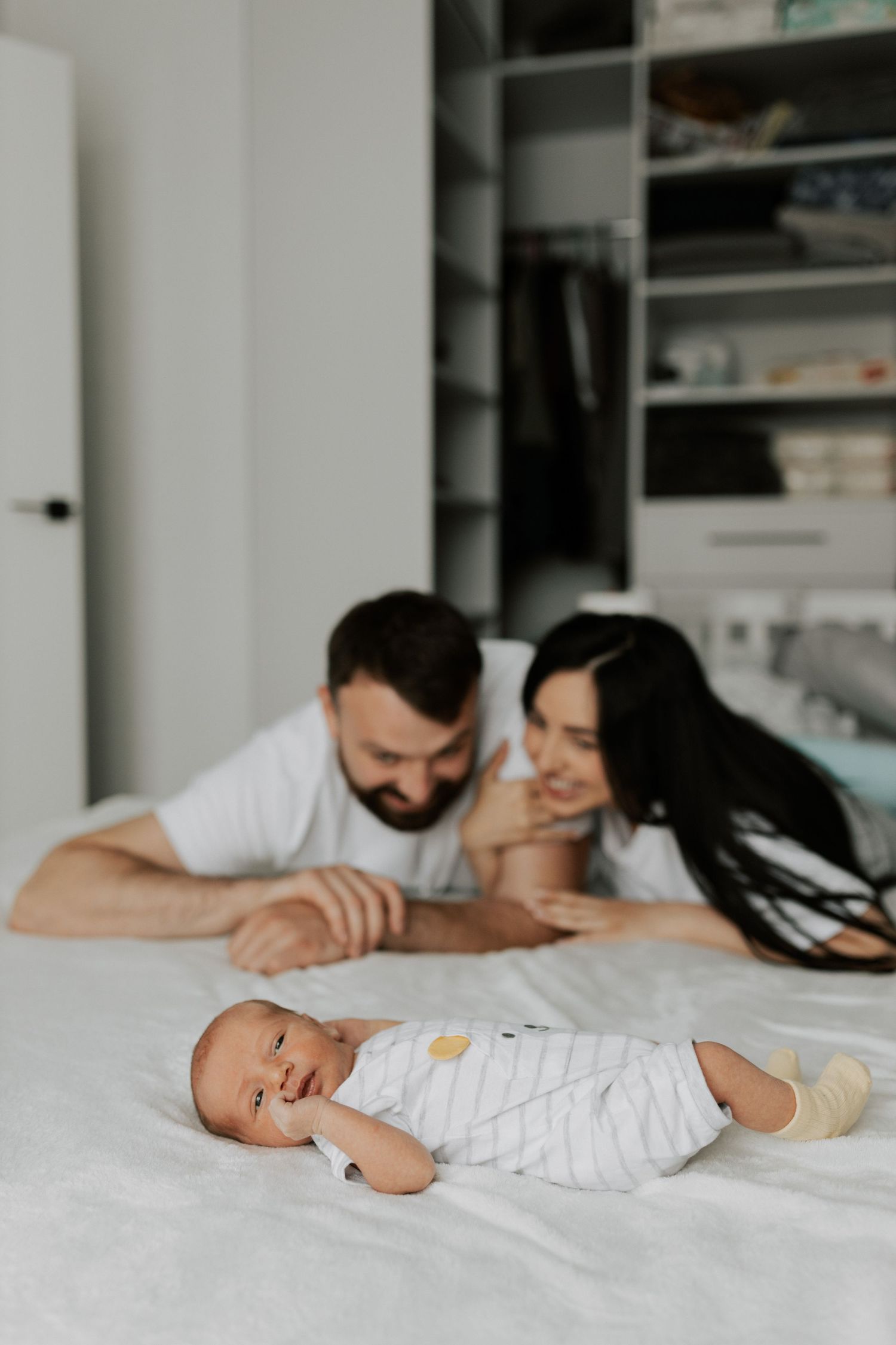 A cozy family moment with parents watching their baby lying on white bedding.