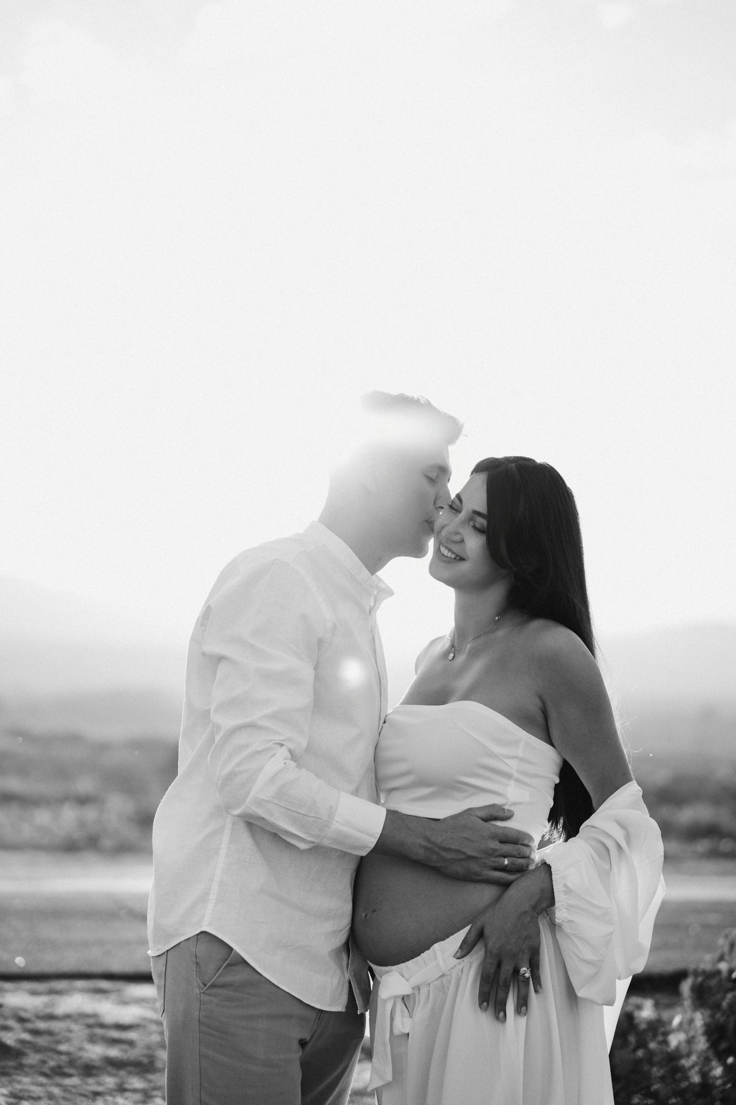Black and white maternity portrait of couple sharing tender moment in natural setting.