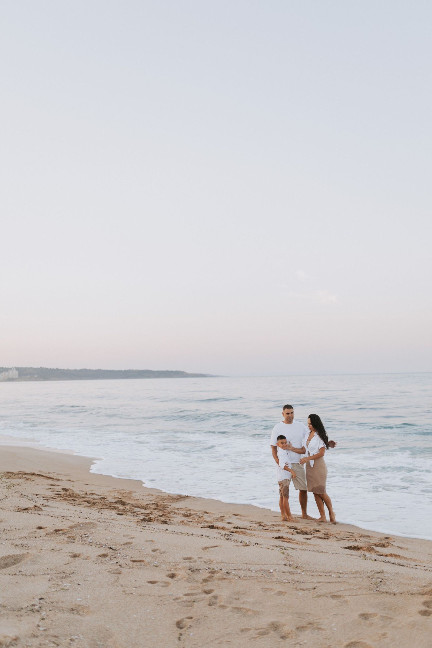 A couple walks along an empty beach shore during golden hour with waves rolling in.