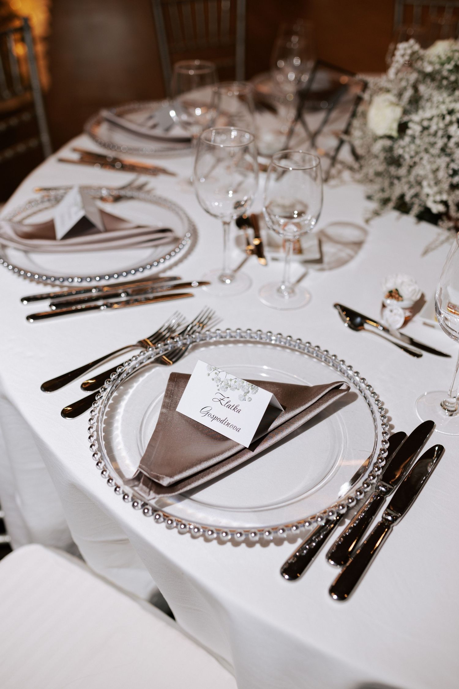 Close-up of formal table setting with beaded charger plate and folded napkin on white tablecloth.