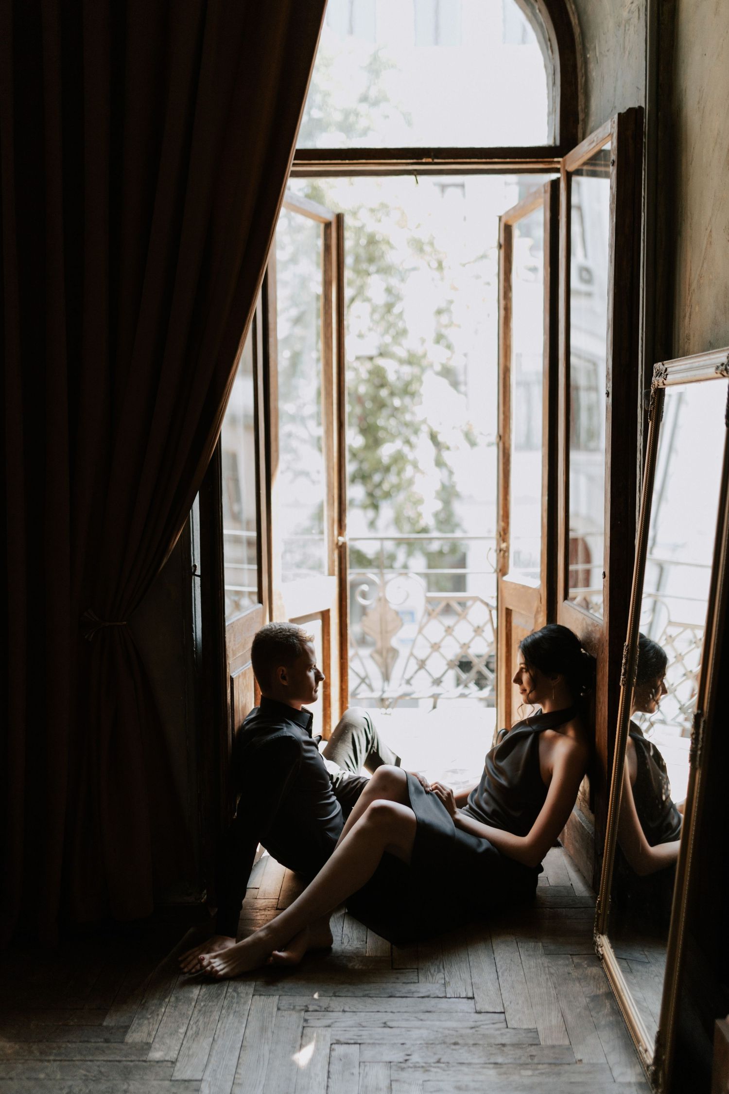 Two people sit in window frame of old building with natural light streaming in.