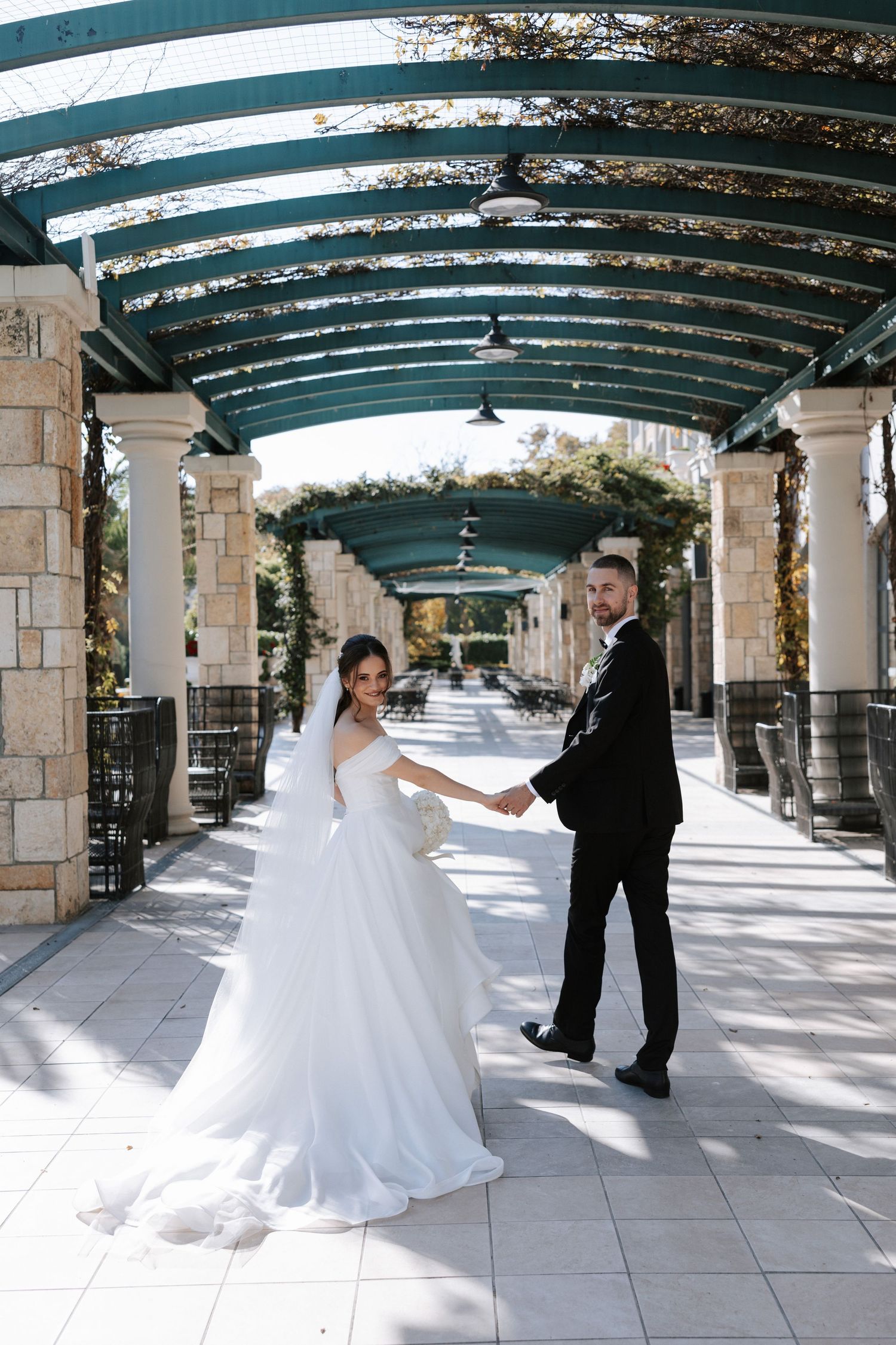 Wedding couple posing under a beautiful covered colonnade with arched green ceiling.