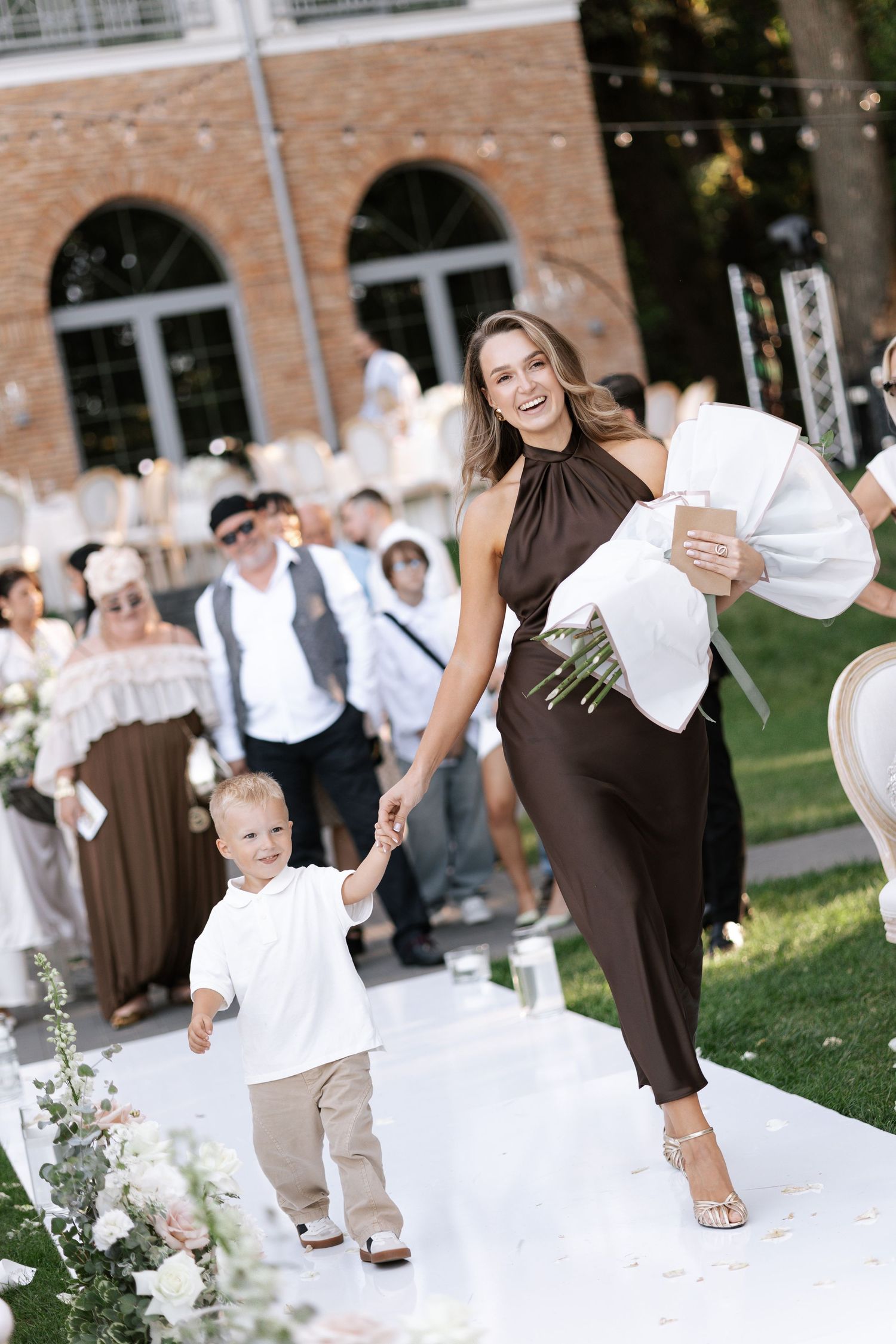 Wedding guests in brown and white attire dancing together on an outdoor patio.