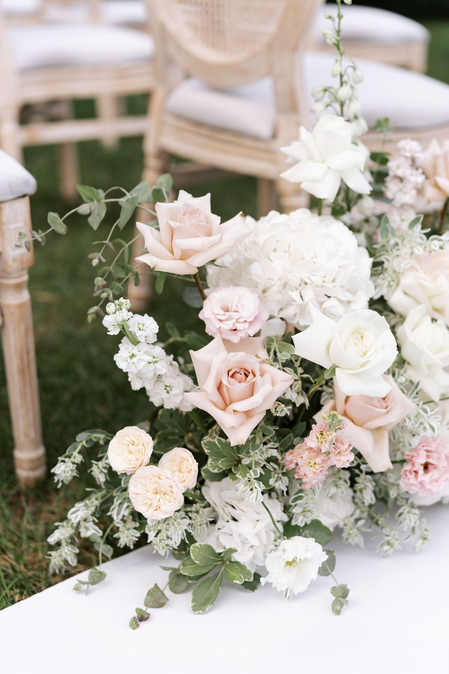 Elegant floral arrangement with blush roses and white flowers adorned with eucalyptus leaves on a table setting.