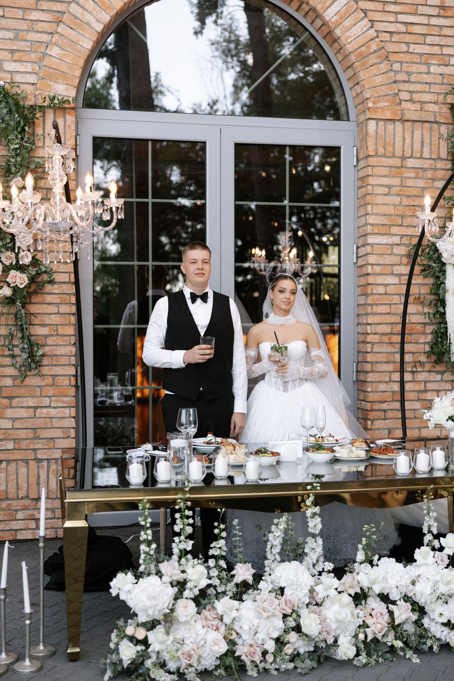 An elegant bar setup with floral decorations and chandeliers at a wedding reception venue.