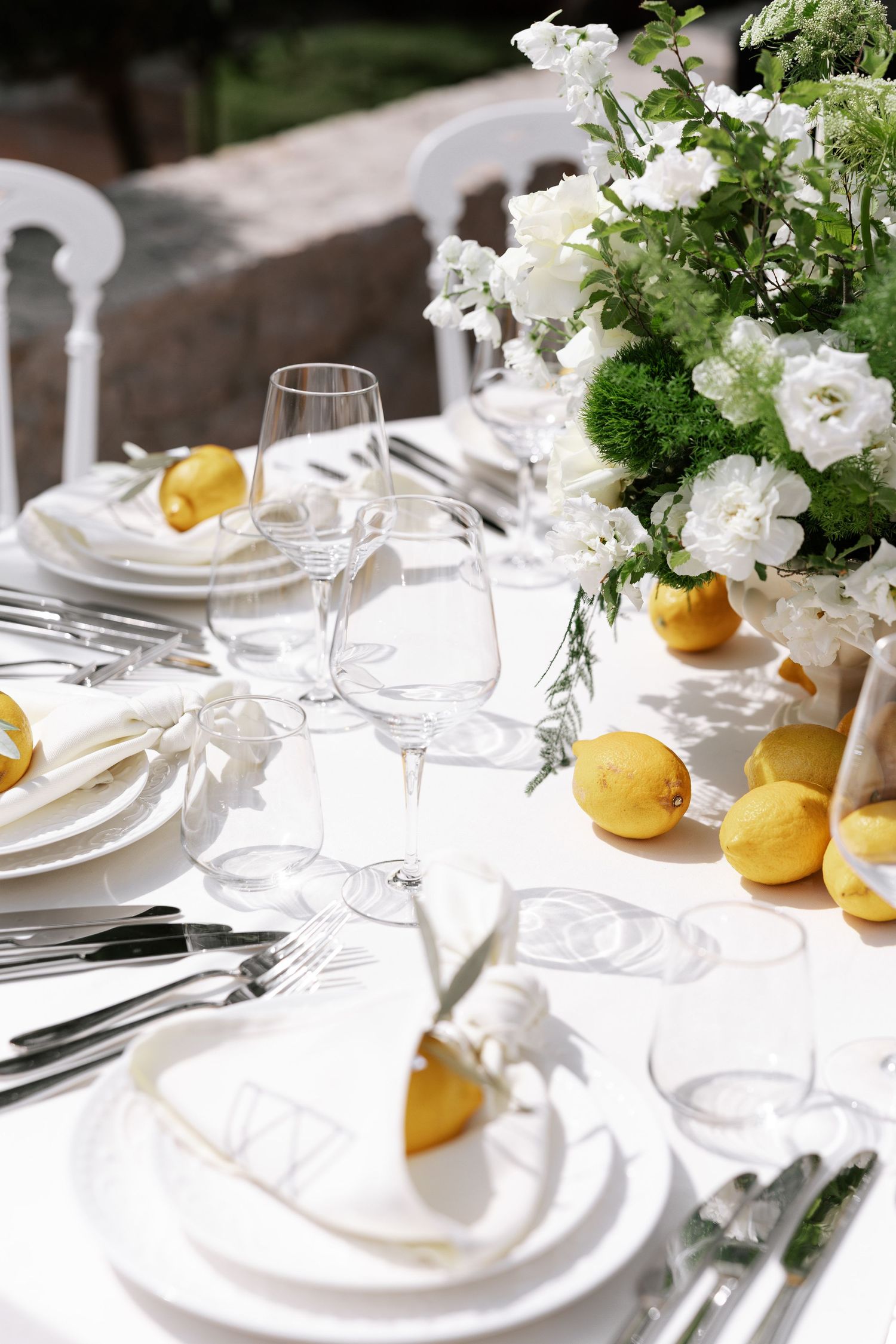 Elegant white table setting with fresh flowers, lemons, and crystal glassware arranged for a formal dining occasion.