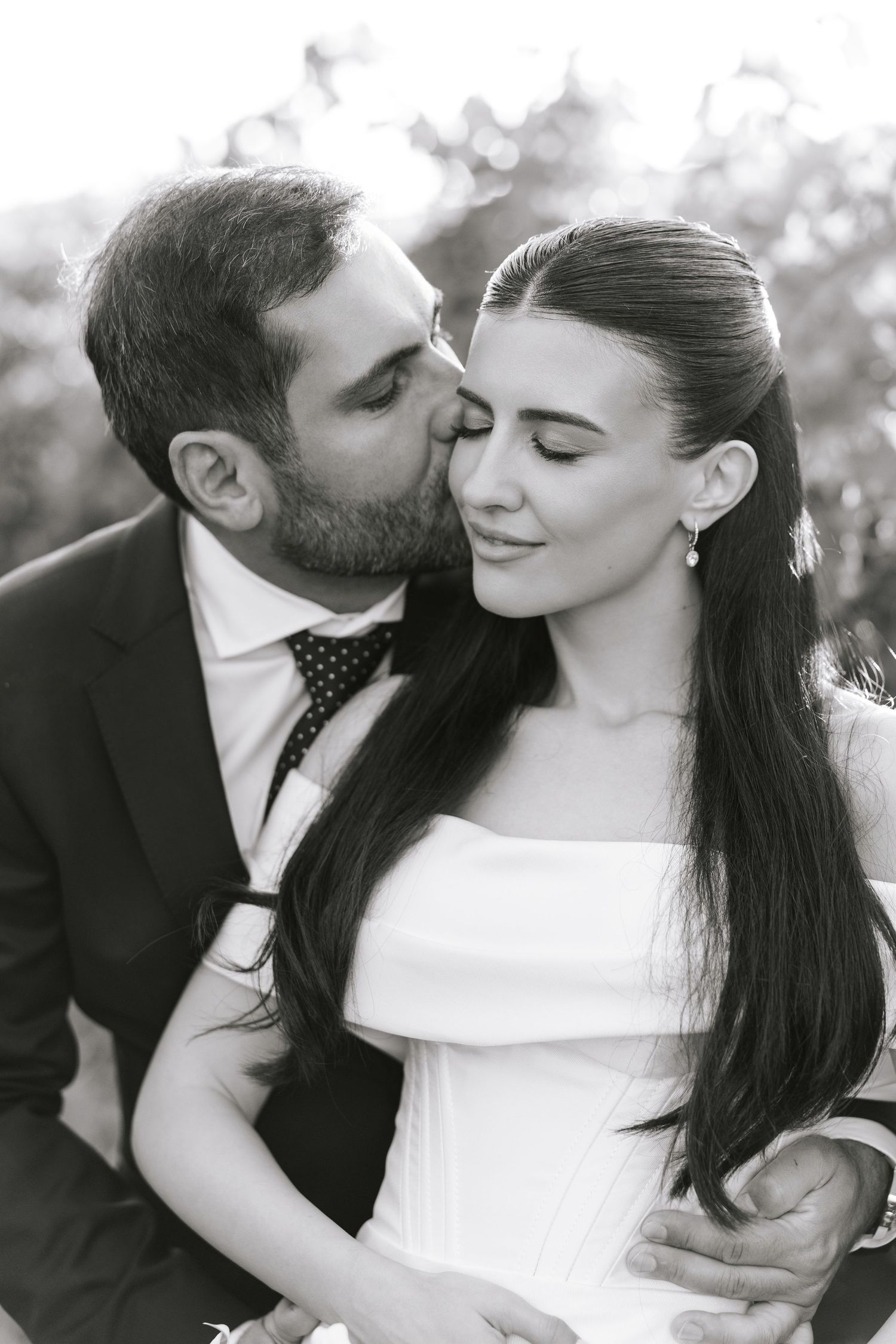 Black and white romantic wedding portrait showing tender moment between couple in formal attire outdoors.