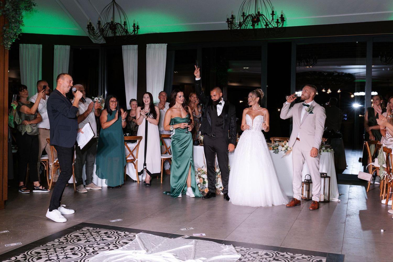 Wedding guests dance and celebrate on an illuminated dance floor during an evening reception at an indoor venue.