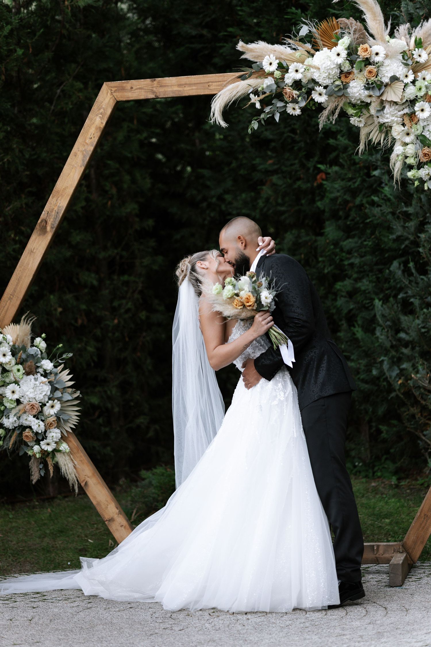 Romantic wedding couple shares intimate moments in front of wooden hexagon arch decorated with white floral arrangements.