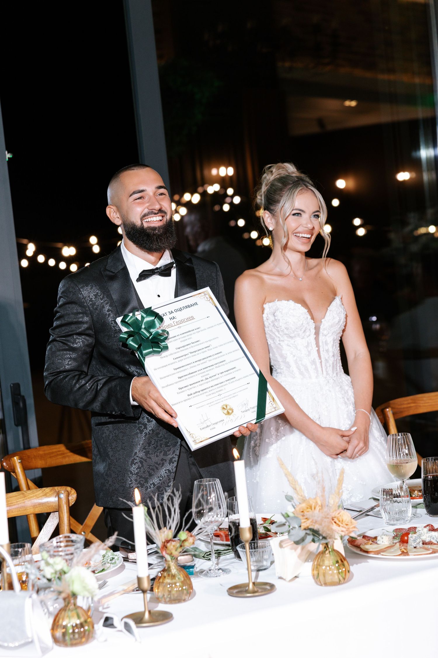 Wedding guests smile and celebrate at an evening reception table decorated with glowing centerpieces.