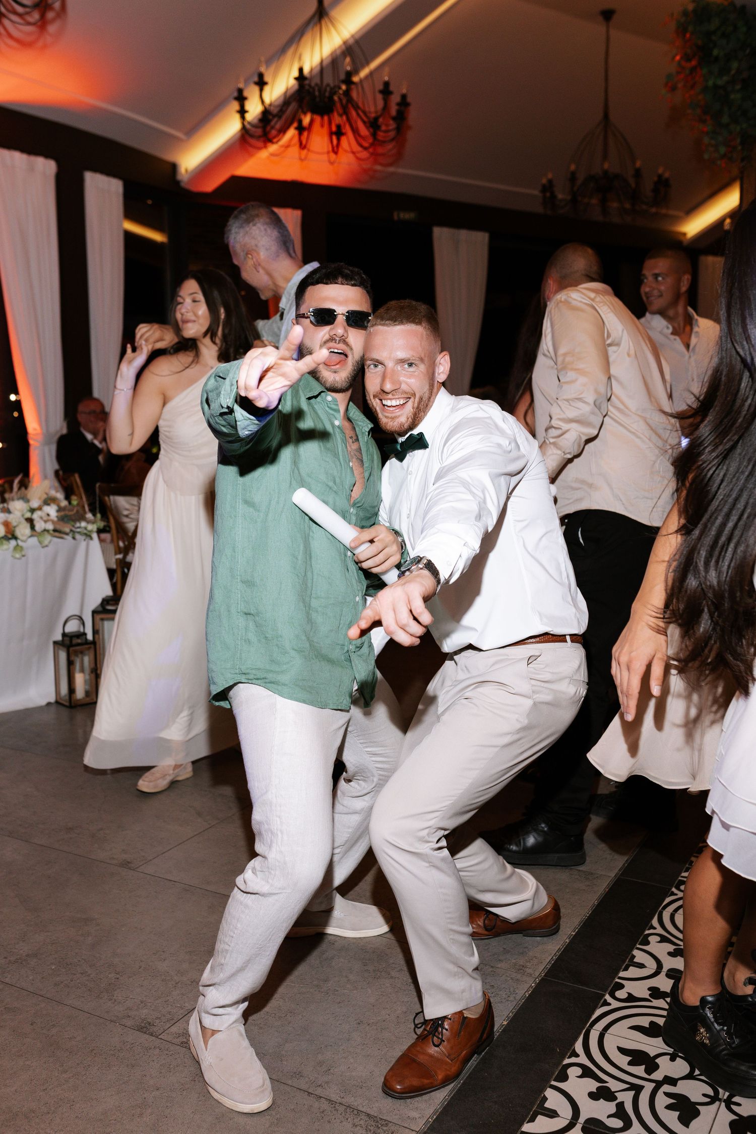 Two party guests dancing and posing enthusiastically on a dance floor at a wedding reception.