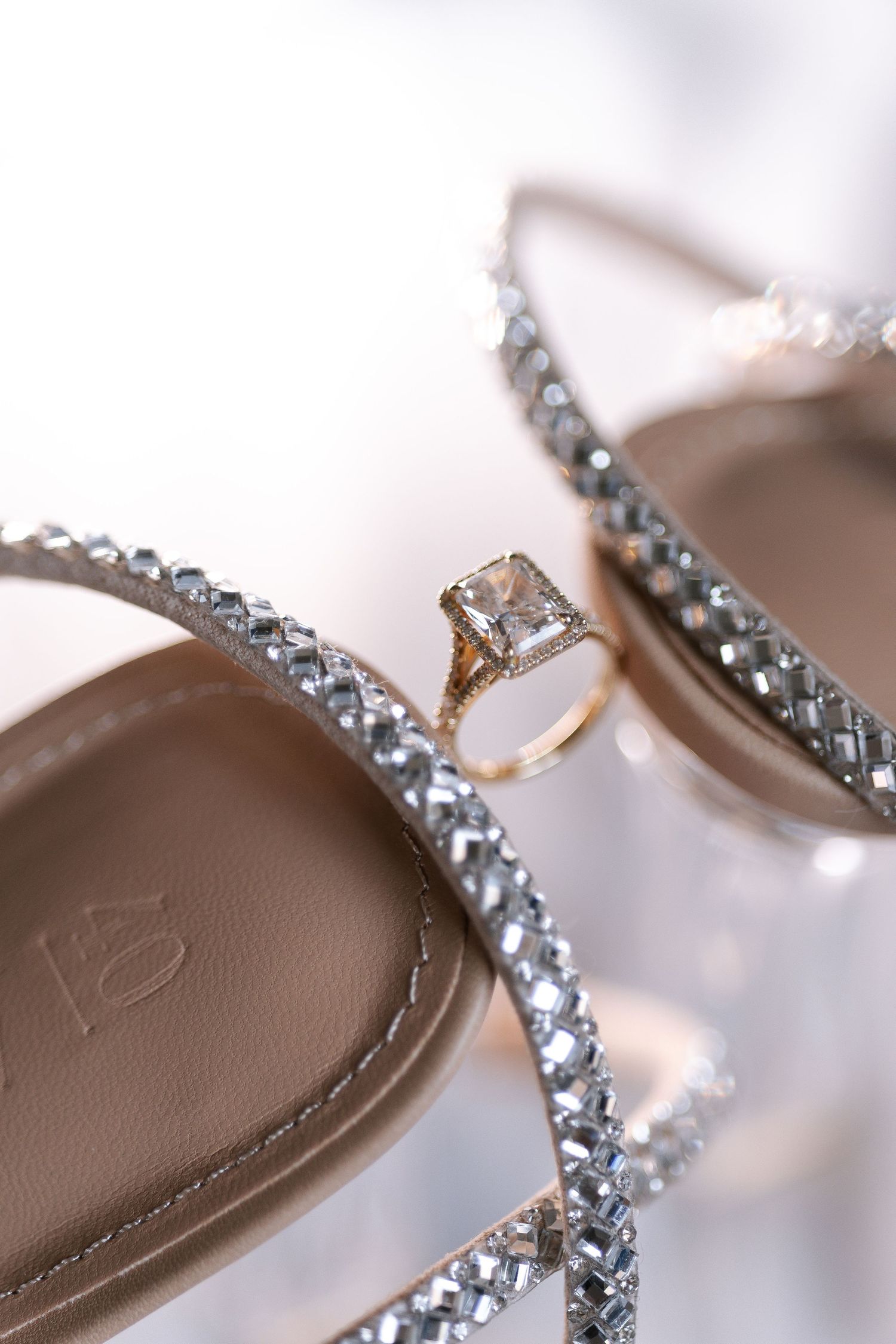 Diamond engagement ring rests elegantly on crystal-embellished bridal shoes in soft focus.