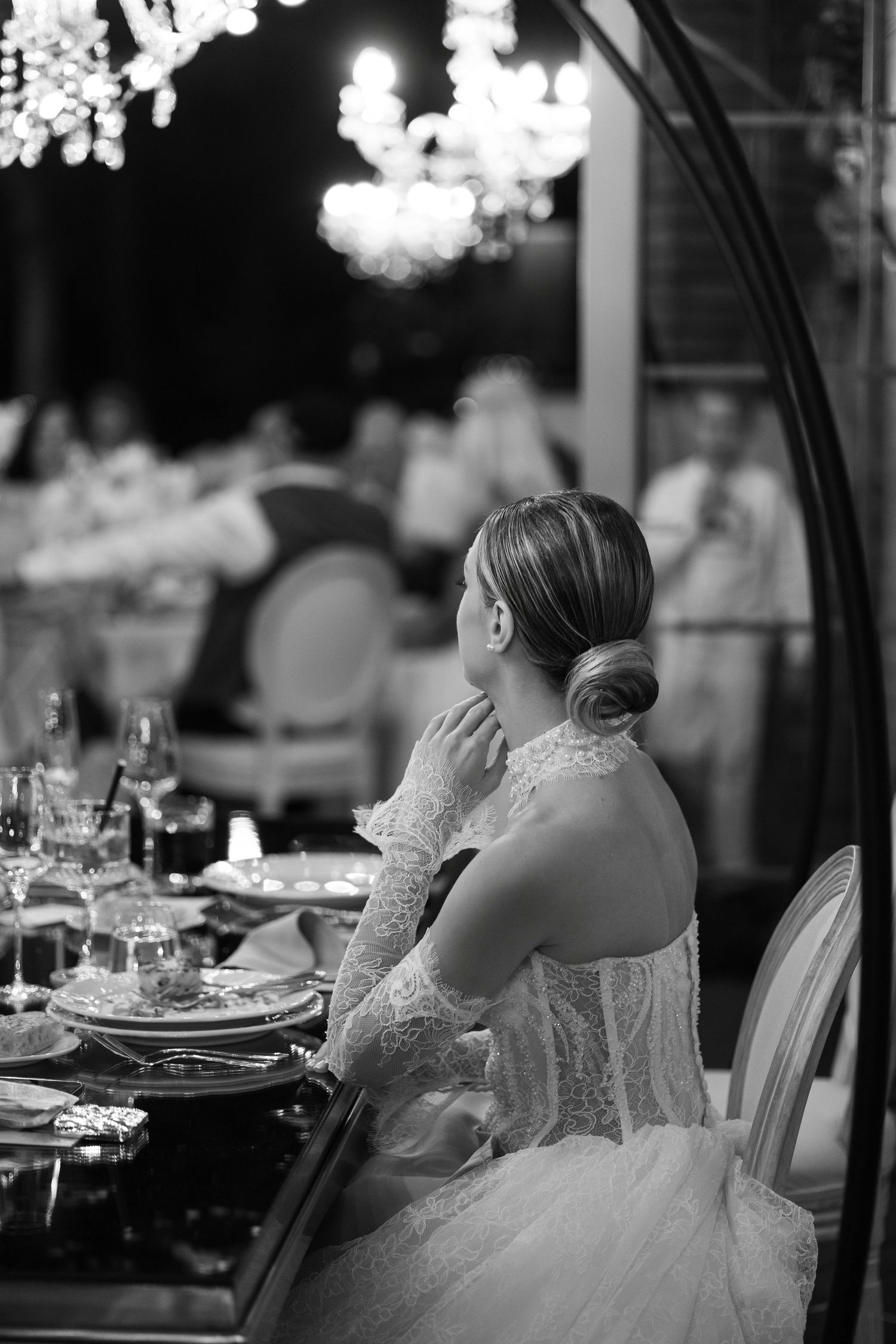 Black and white photo of an elegant wedding reception with crystal chandeliers and formal table settings.