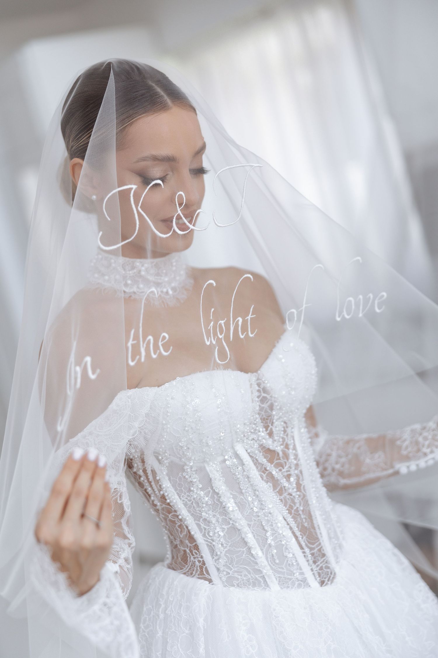 A bride in a stunning white lace wedding dress with sheer details and a flowing veil poses elegantly.