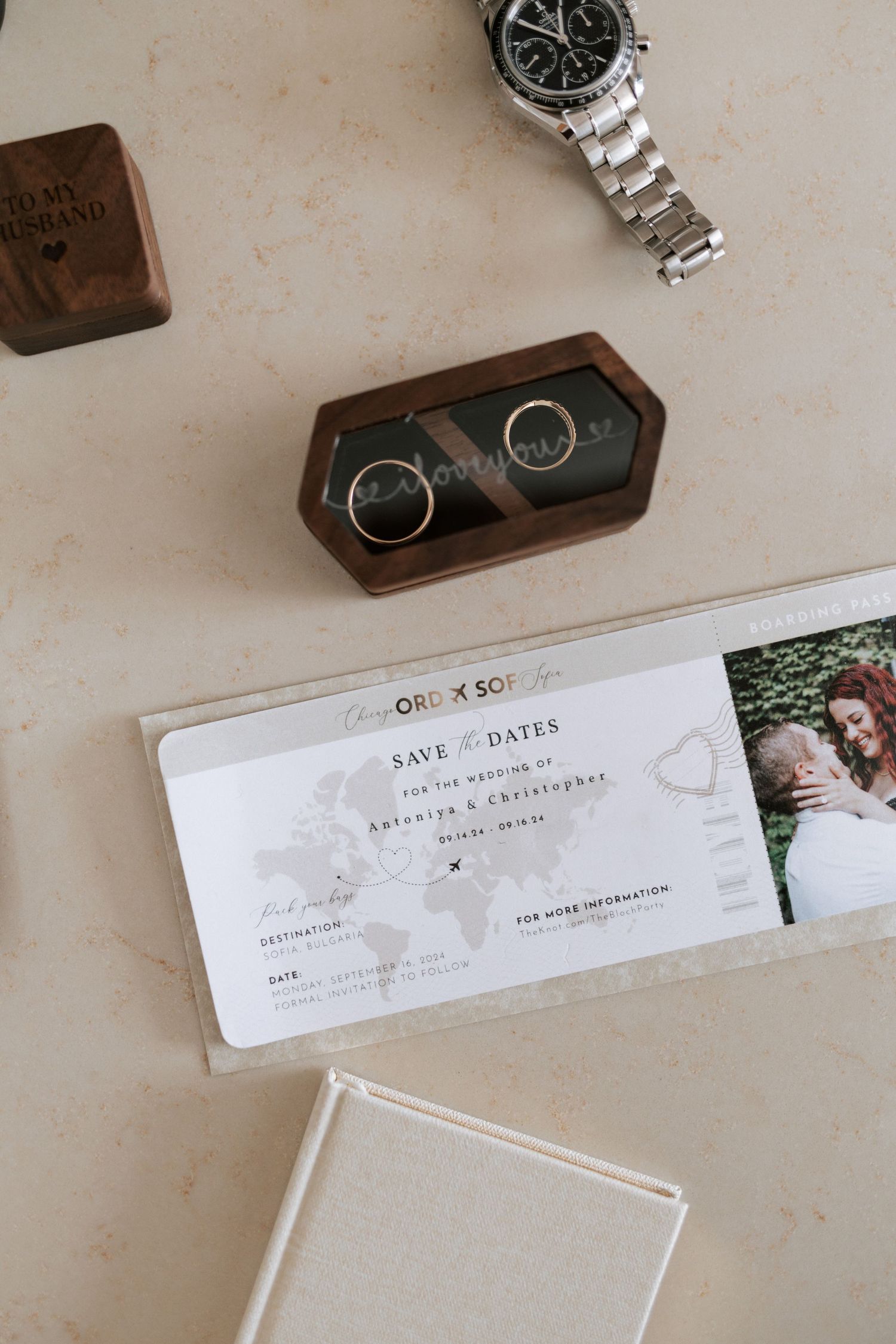 Wedding details arranged on table including silver watch, wooden ring box and save the date card.