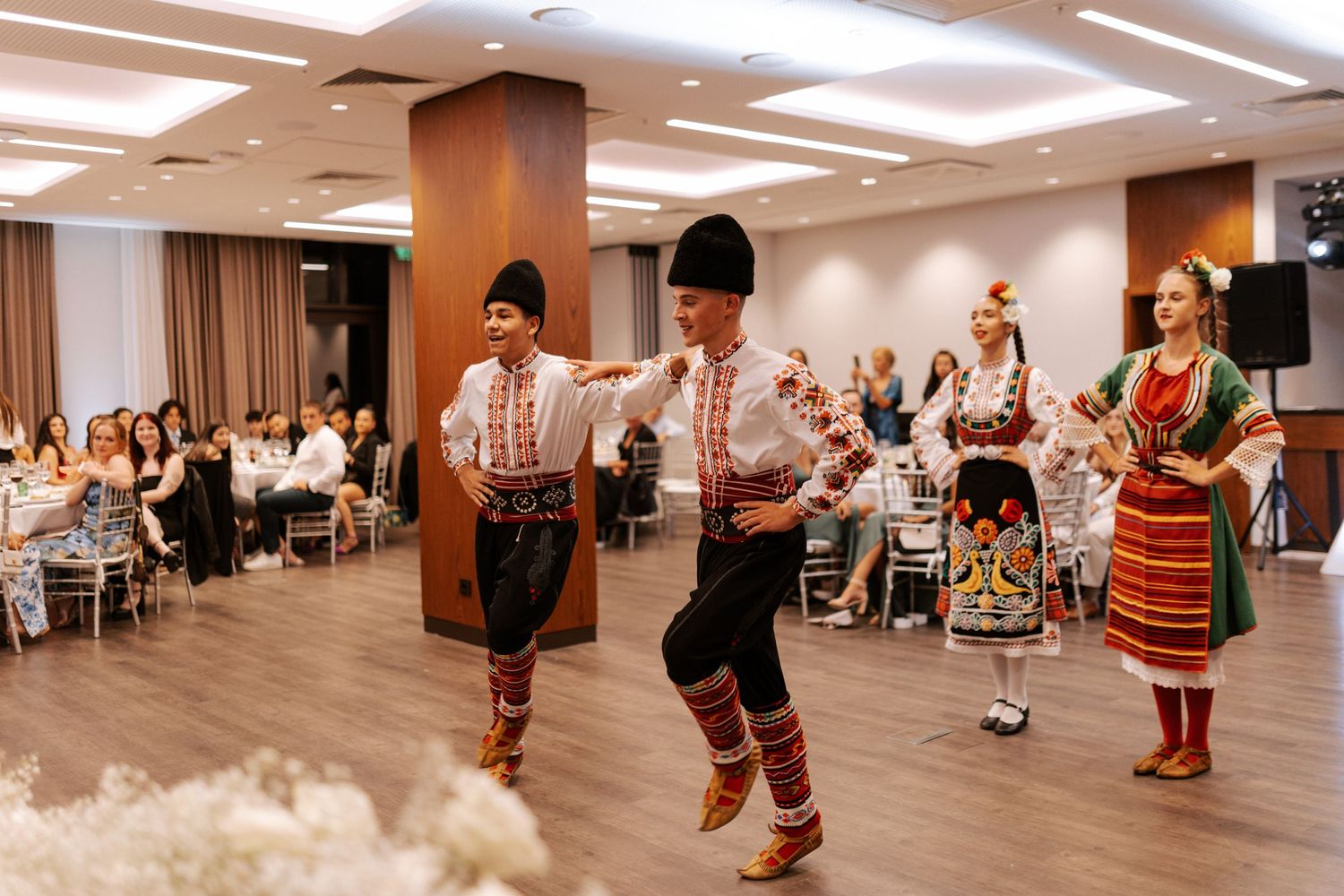 Traditional folk dancers performing in colorful costumes at a wedding reception.