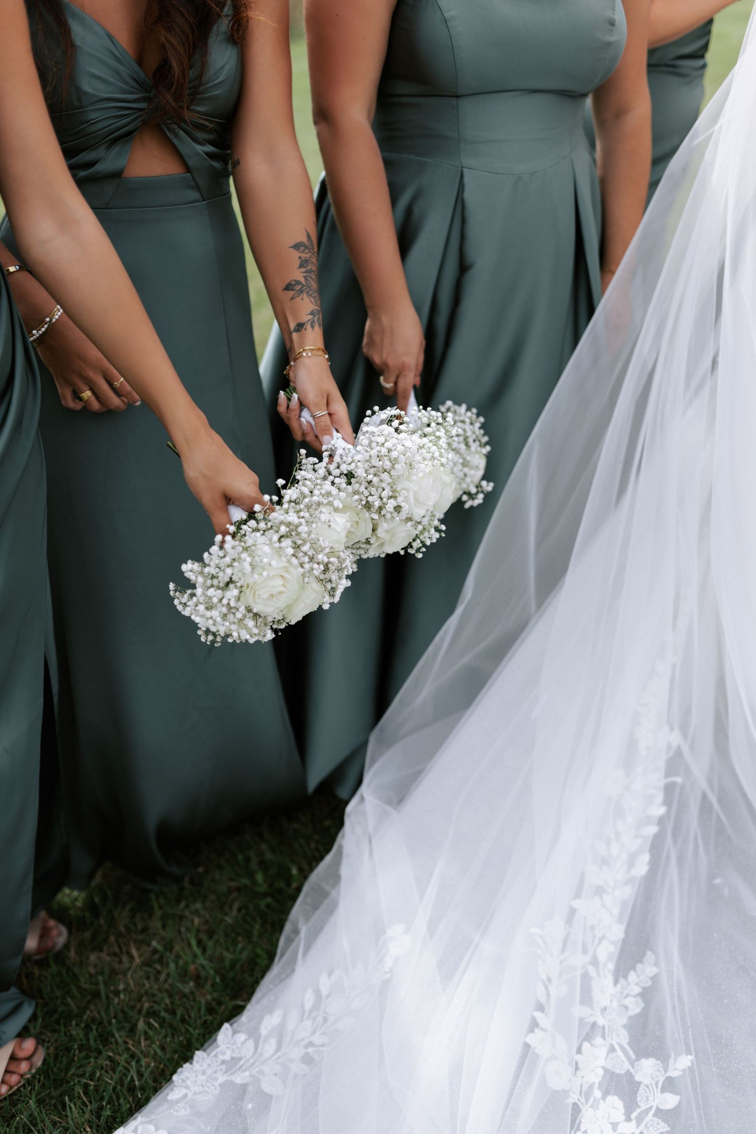 Close-up of white bouquets held against sage green bridesmaid dresses and bridal gown.