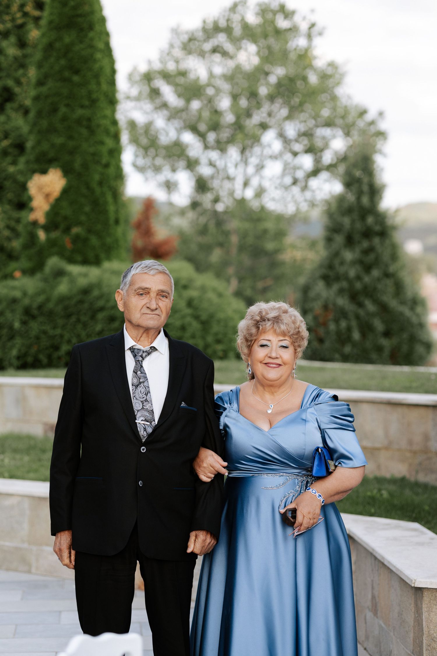 Elegant couple in formal attire poses in garden setting.