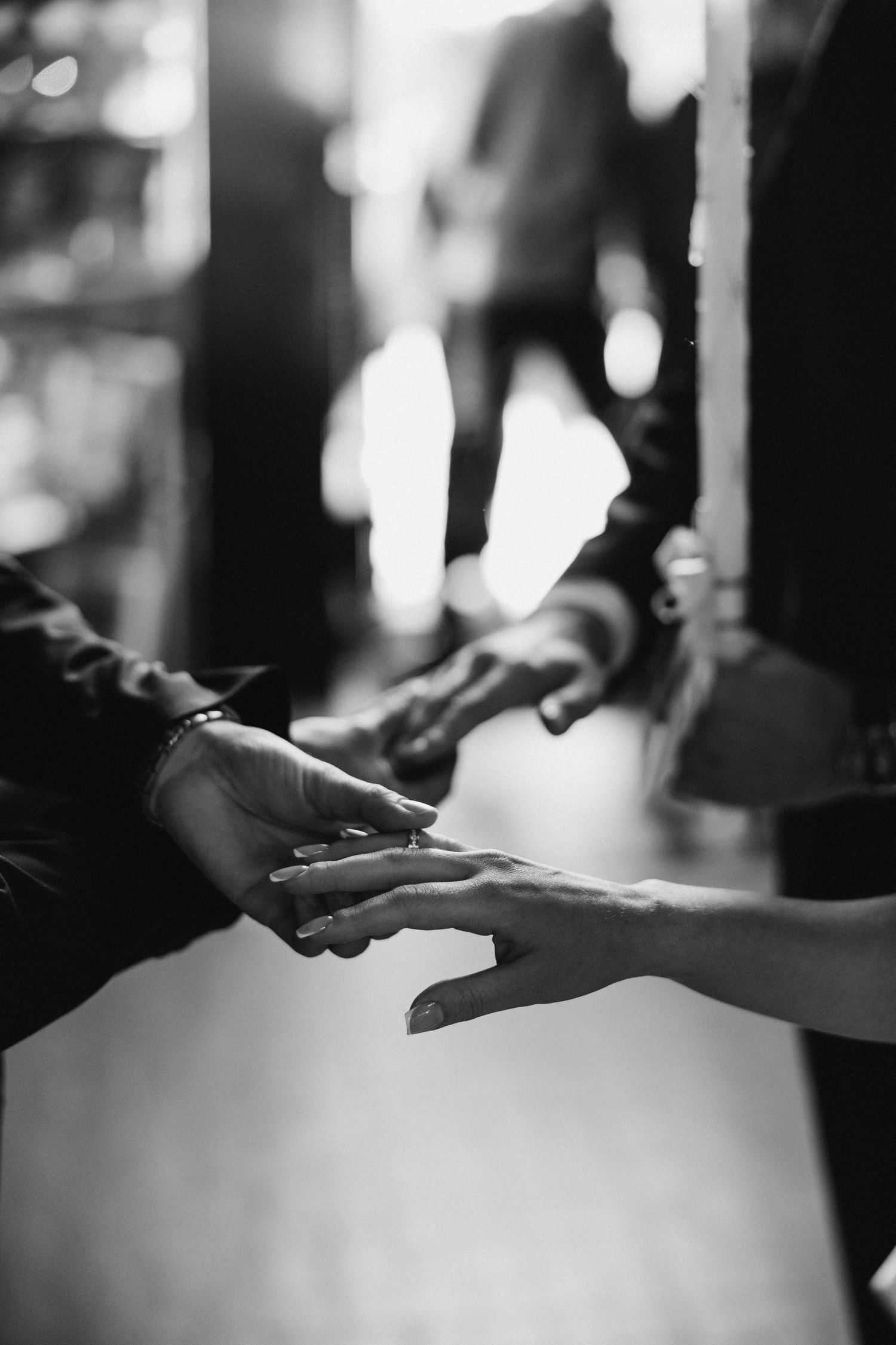 Black and white closeup of hands exchanging wedding rings during ceremony.