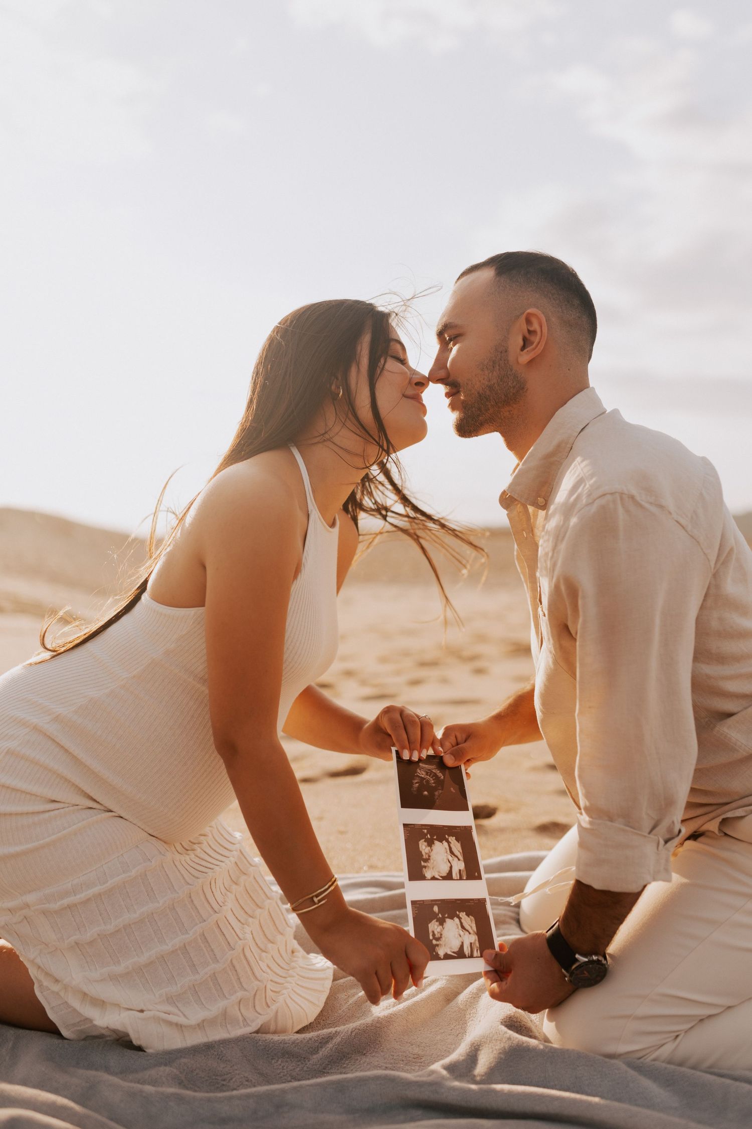 A couple sharing an intimate moment on the beach while holding ultrasound photos.