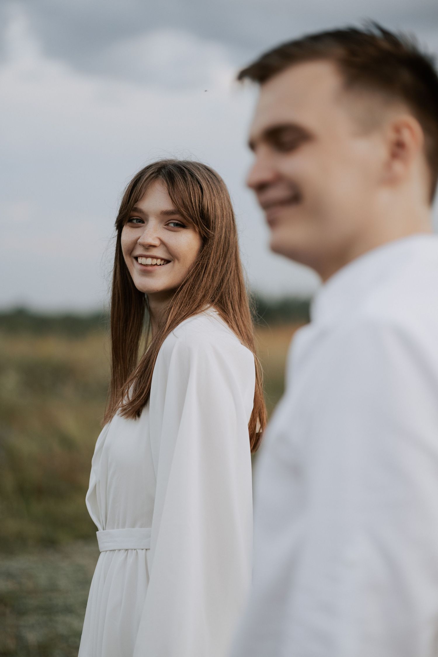 Side profile of couple in white clothing smiling during outdoor countryside photoshoot.