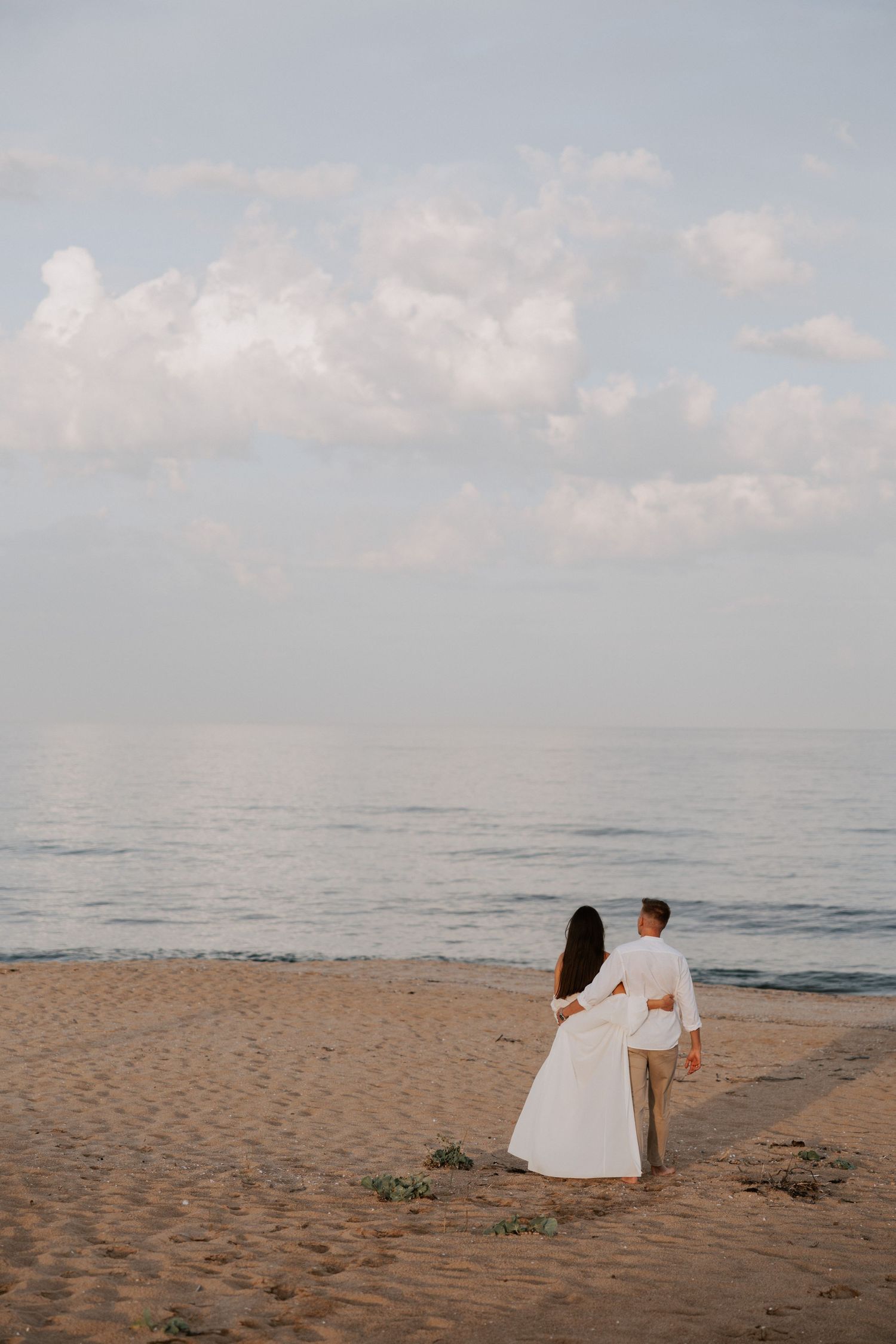Couple in white stands on beach shoreline during sunset.