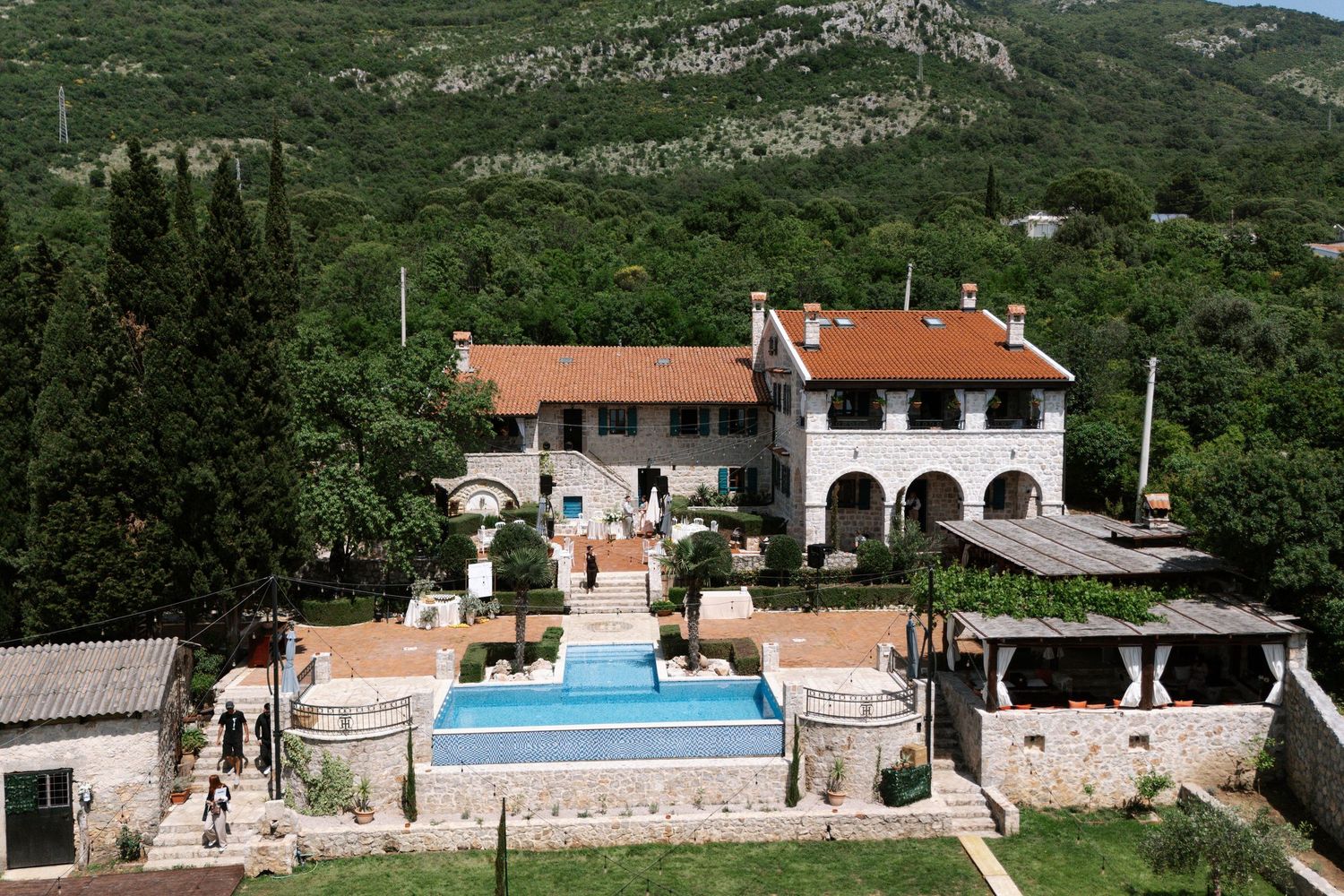 Aerial view of a Mediterranean villa with terracotta roof and swimming pool nestled in lush mountainous landscape.