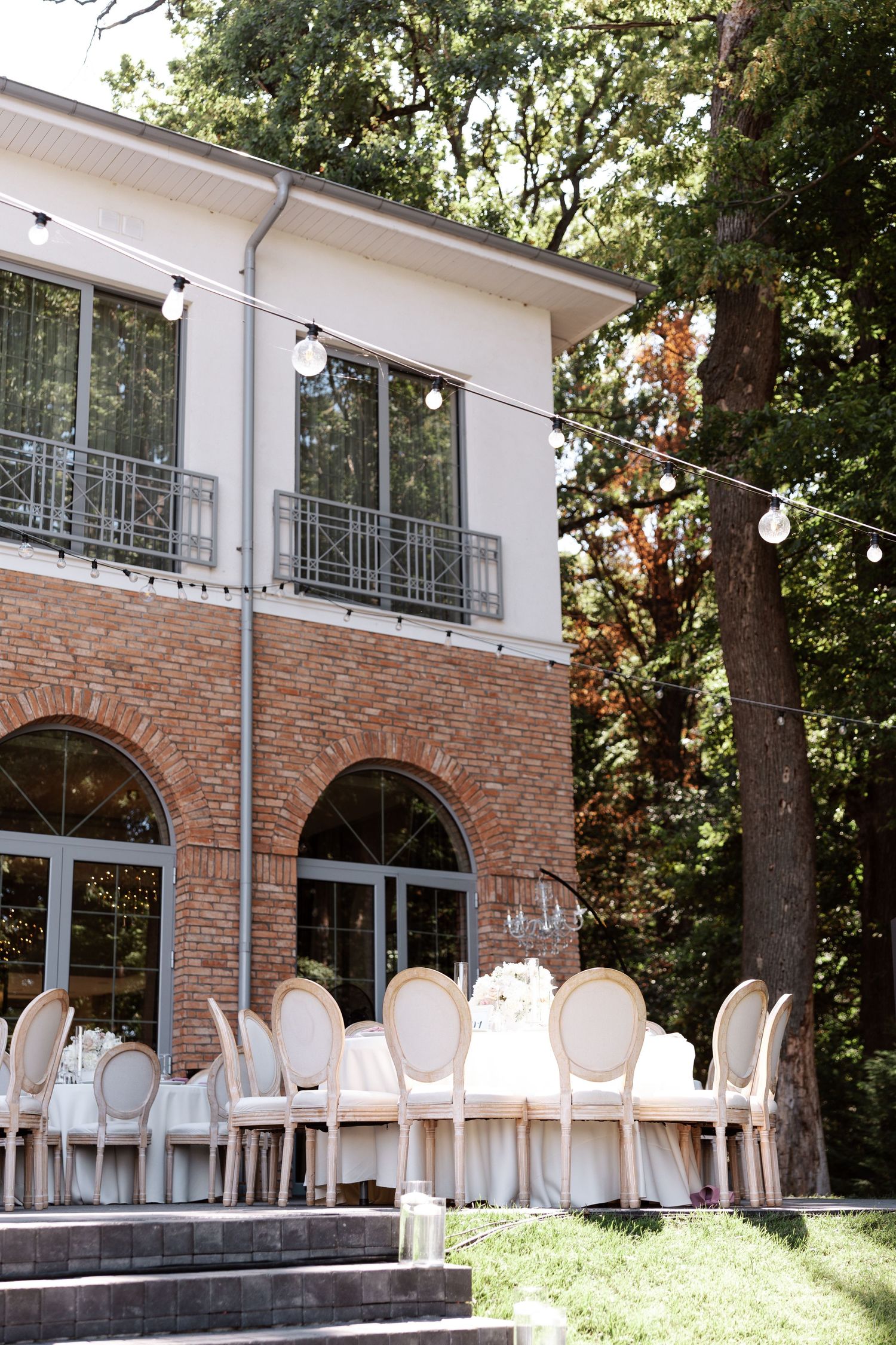 Elegant outdoor wedding venue with white French chairs and brick archways surrounded by lush greenery.