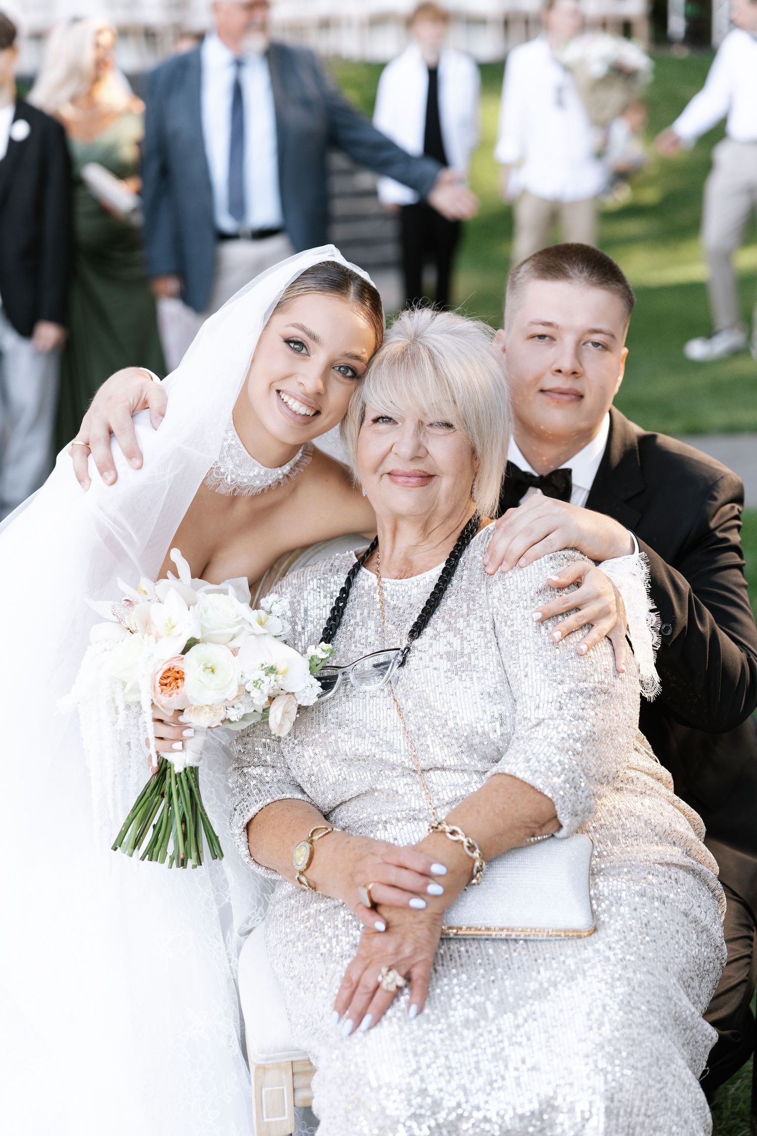 Wedding party members embrace in formal attire against outdoor backdrop.