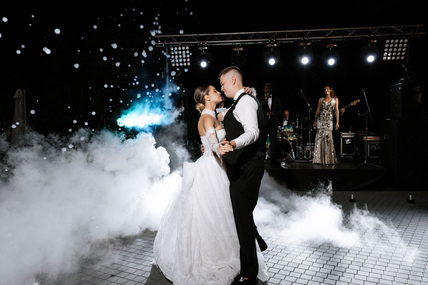 Wedding couple dances in fog effects on illuminated dance floor.