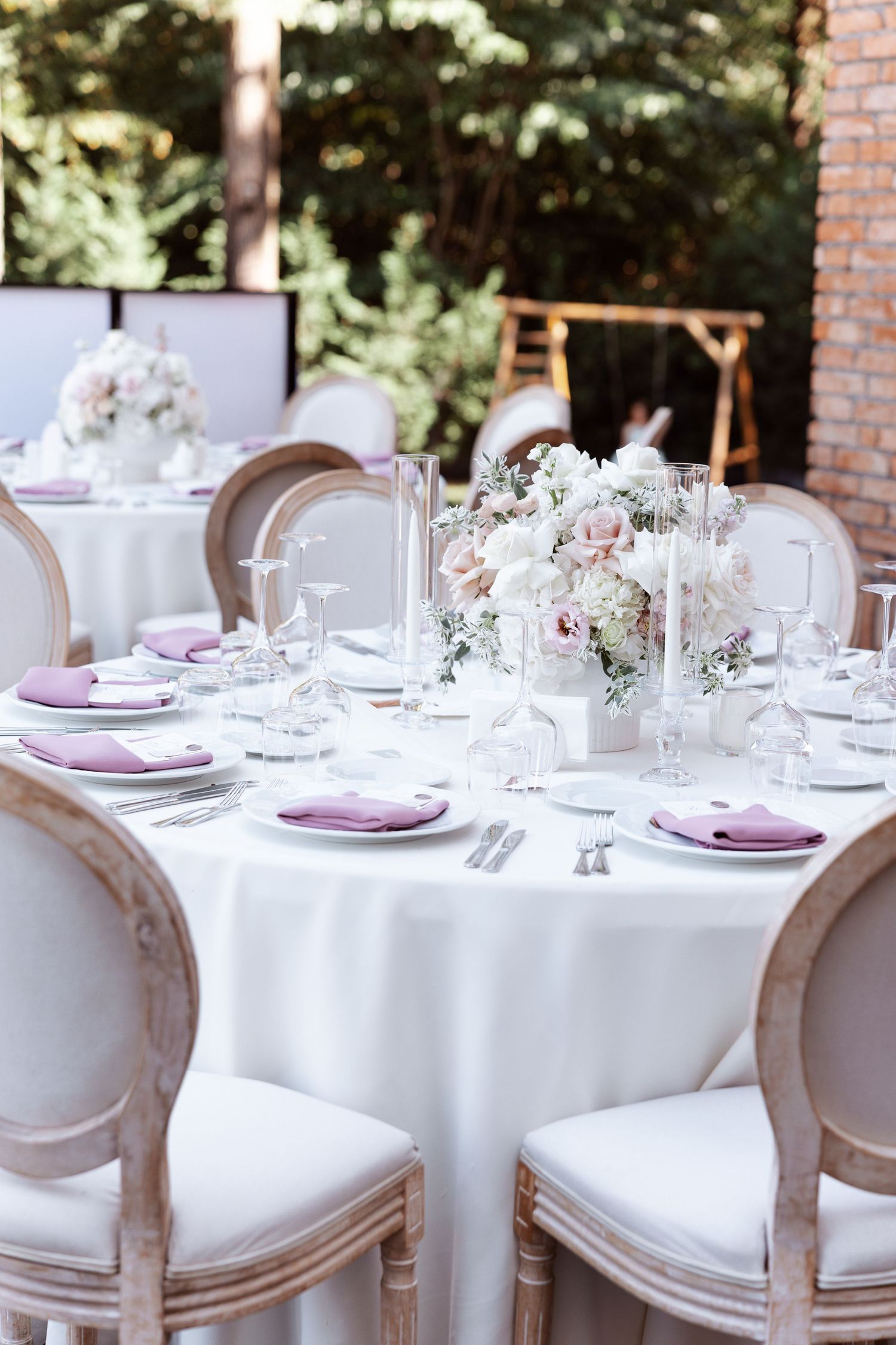 Elegant wedding reception tables set with white linens, purple accents, and delicate floral centerpieces.