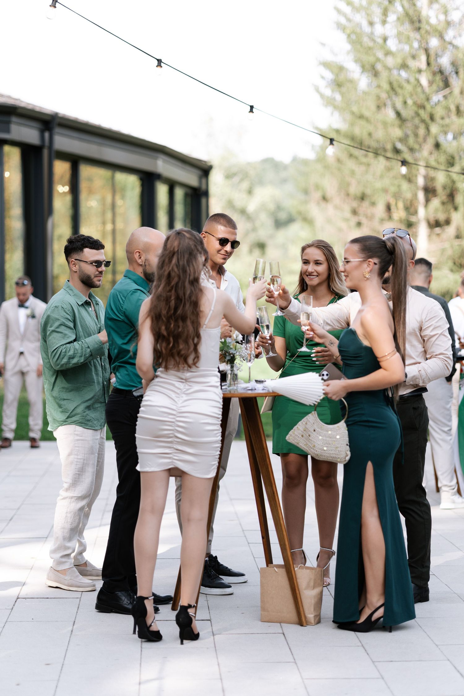 Wedding guests in green and white attire mingle and socialize during an outdoor reception celebration.