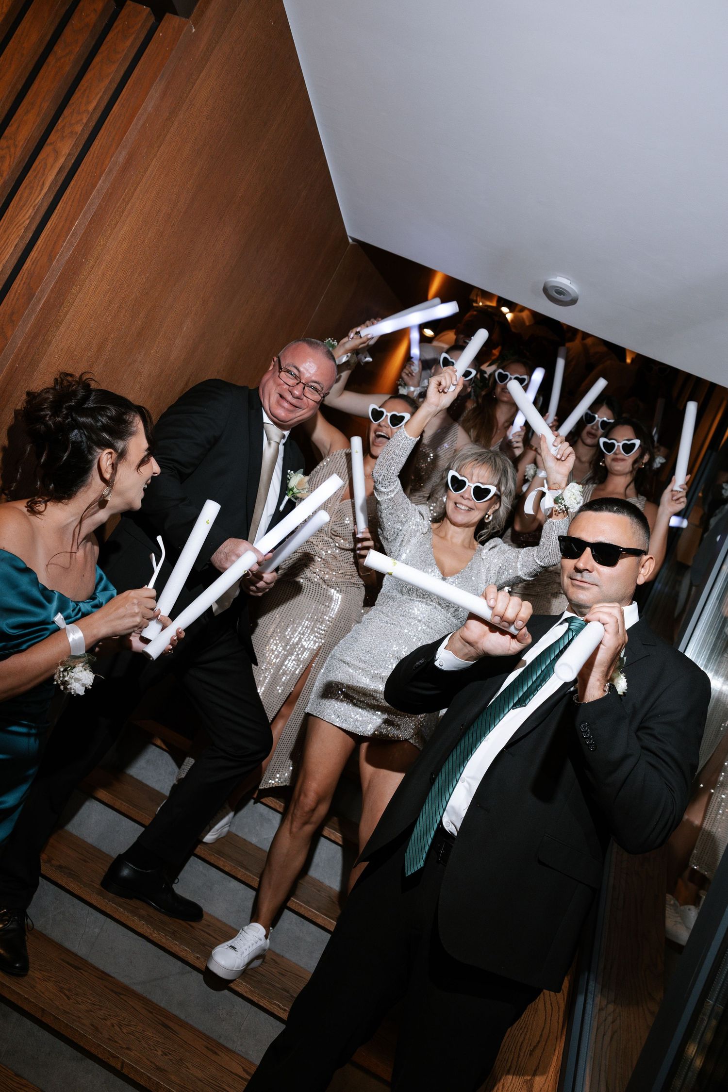 A group in sunglasses poses playfully with glow sticks at what appears to be a party or celebration.