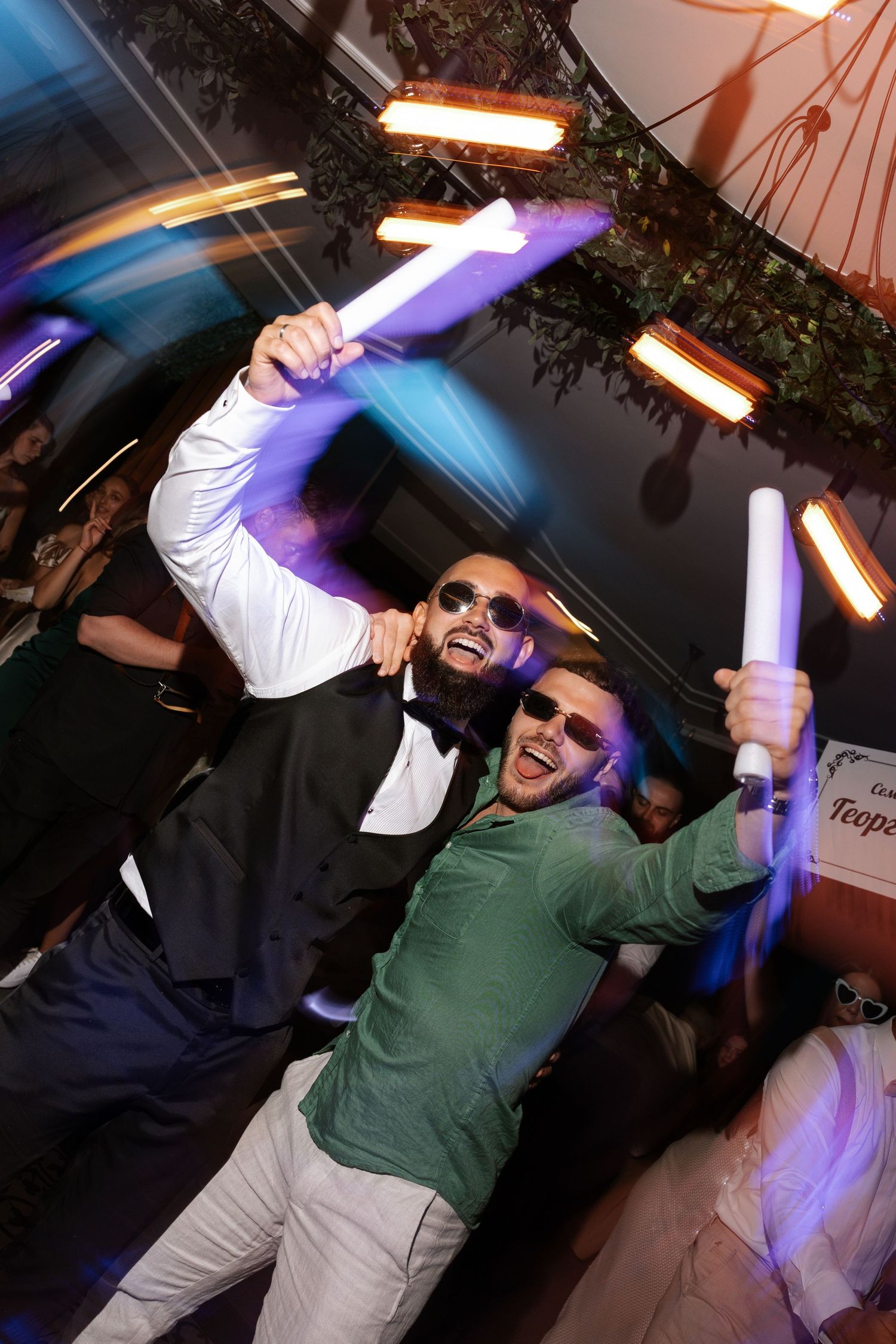 Person in green sweater dancing enthusiastically under colorful party lights on a dance floor.