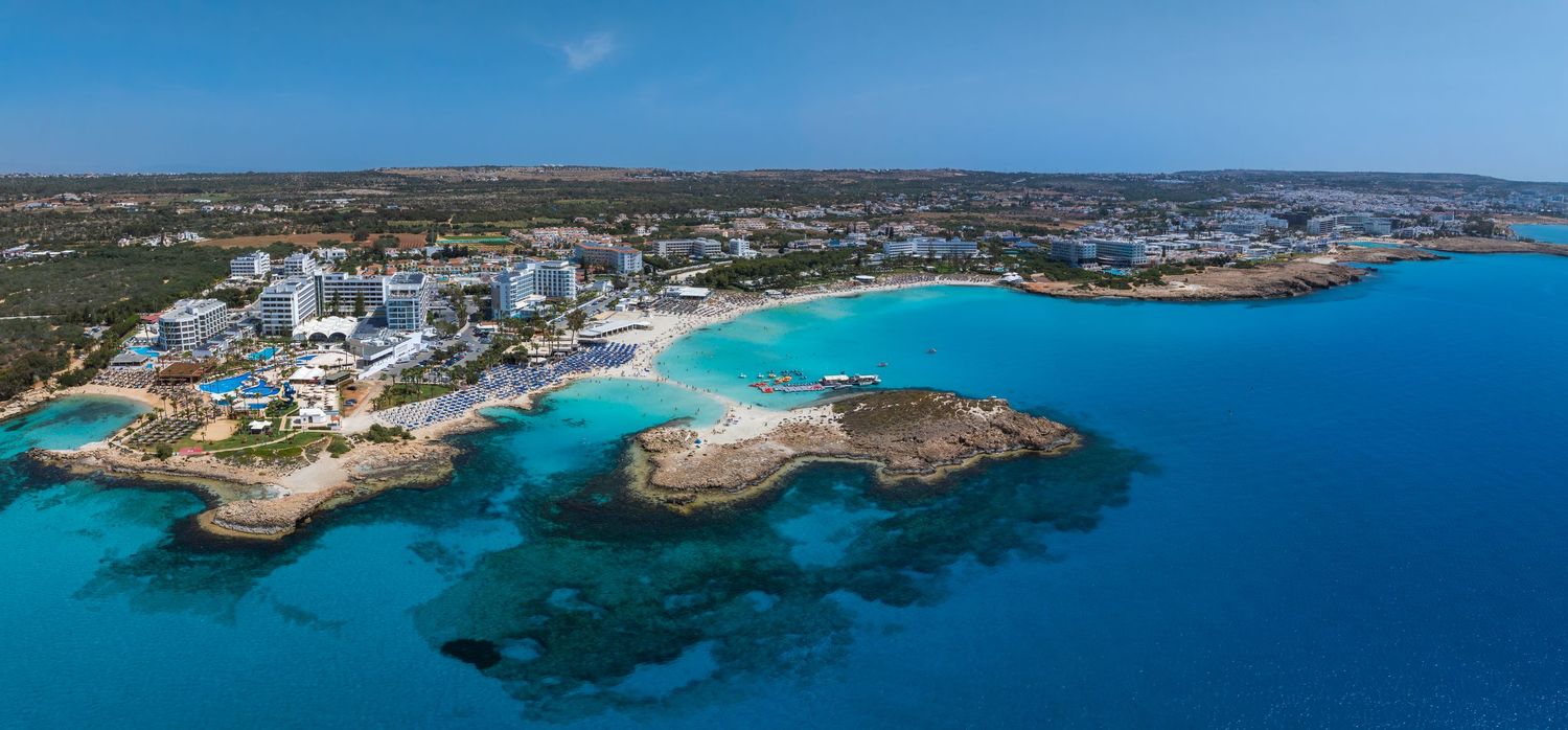 Panoramic coastal landscape showing curved shoreline, beaches and rocky outcrops along blue waters.