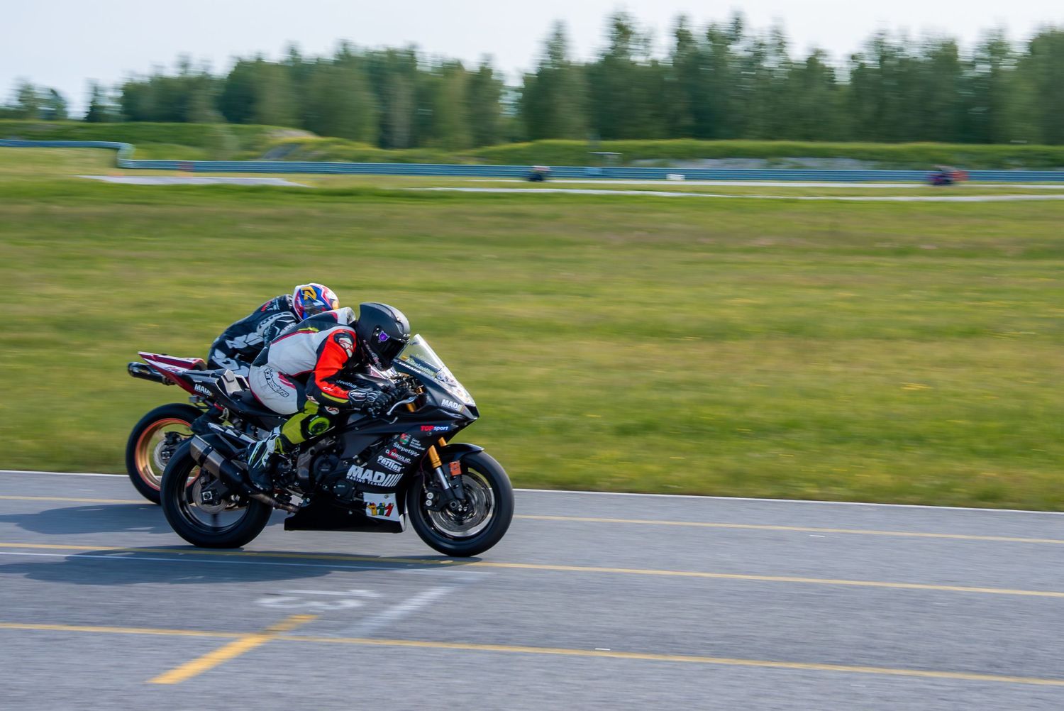 Motorcycle racer leaning into a turn on a race track with grass in the background.