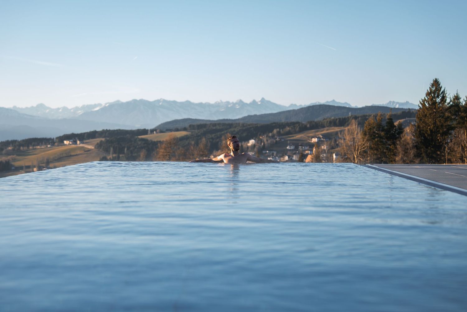 Serene lakefront view with snow-capped mountains in the distance and calm blue waters.