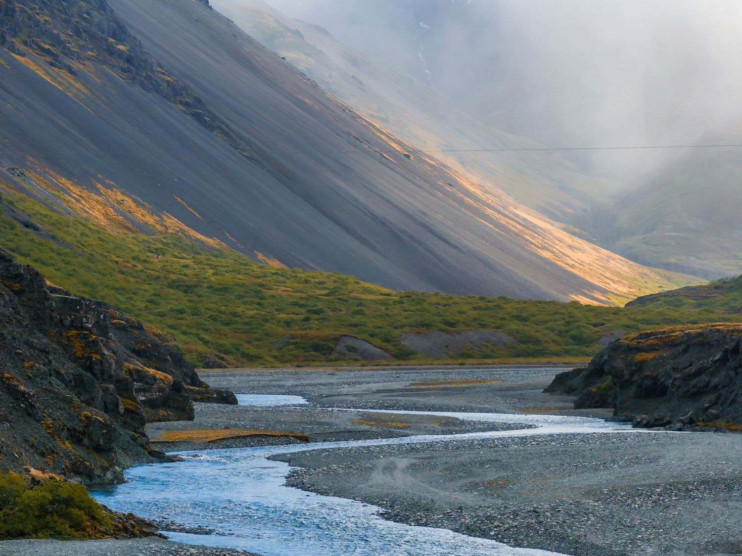 Dramatic mountain valley with winding river and steep slopes in misty conditions.