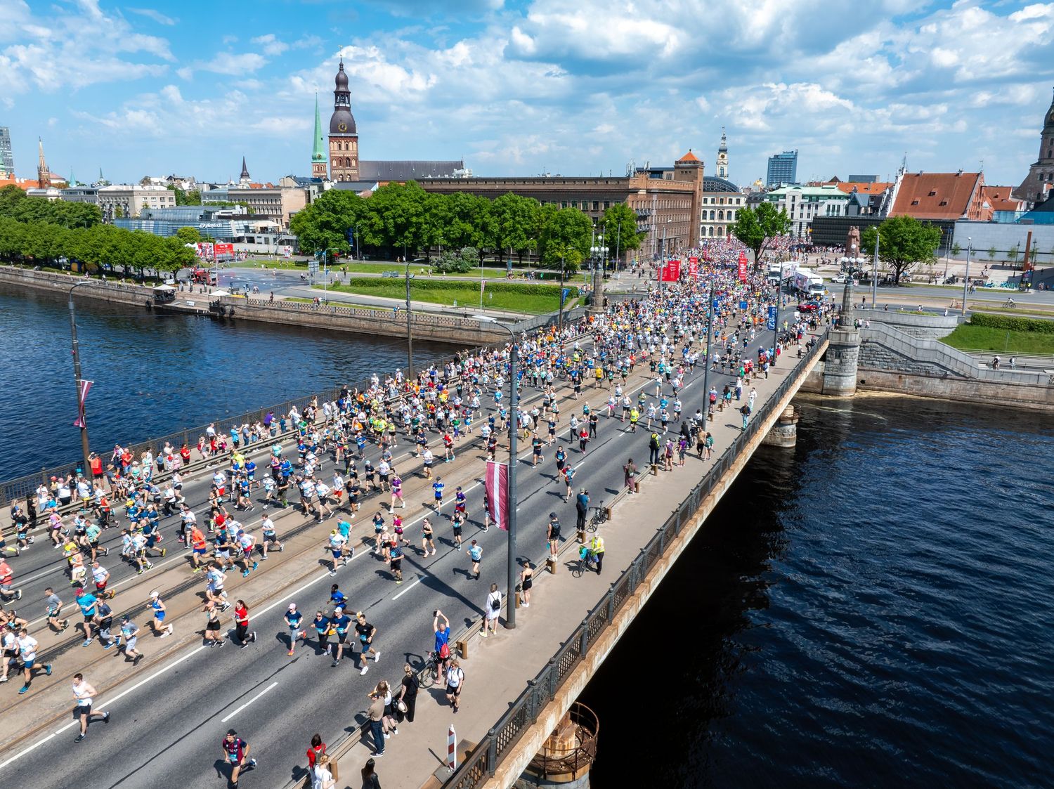 Aerial view of marathon runners crossing a bridge over water with city buildings in background.