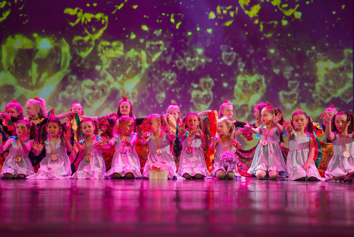 Dance ensemble performs in vibrant pink costumes against a purple-lit stage backdrop.