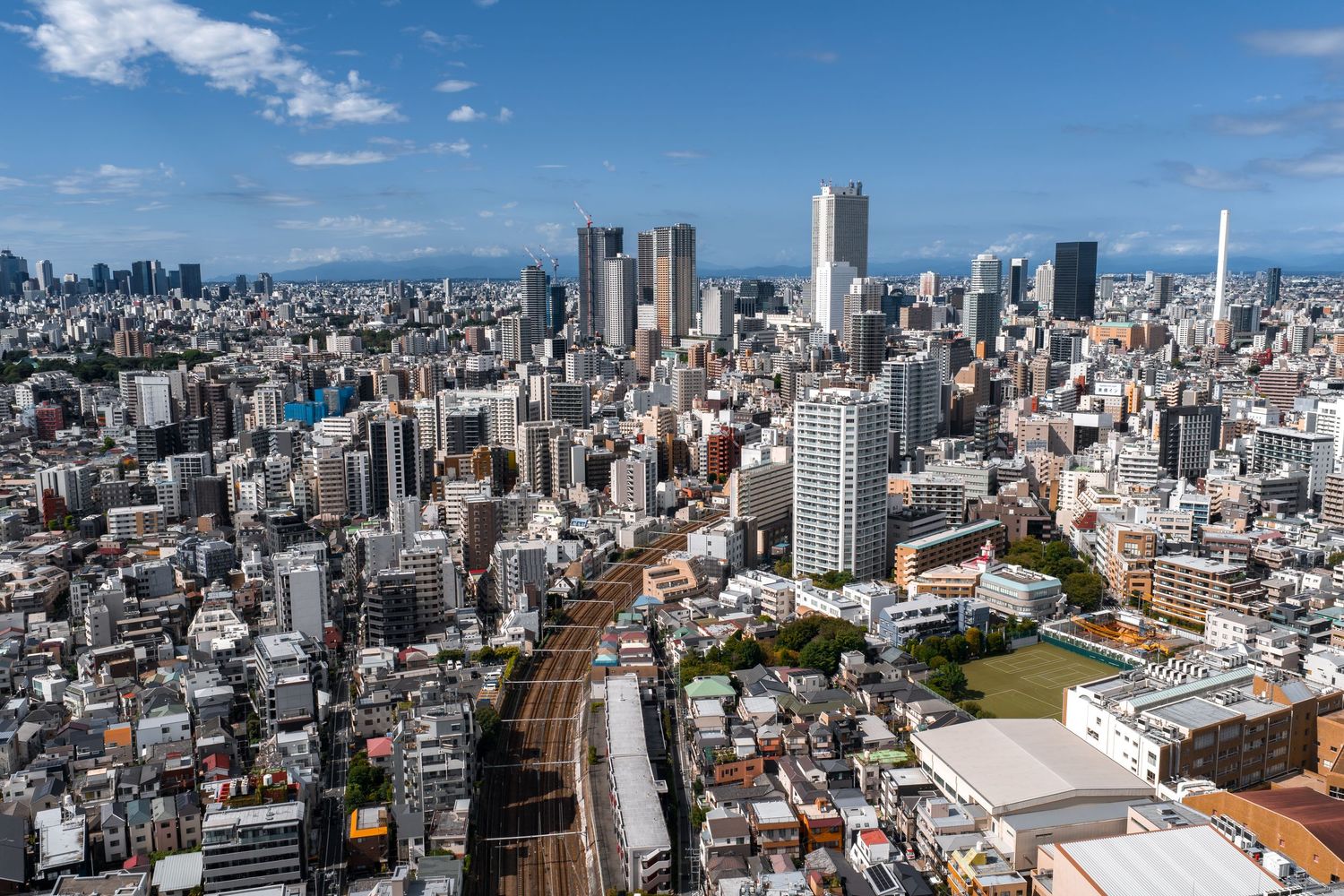 Panoramic aerial view of Tokyo's modern cityscape with skyscrapers and residential buildings under blue sky.