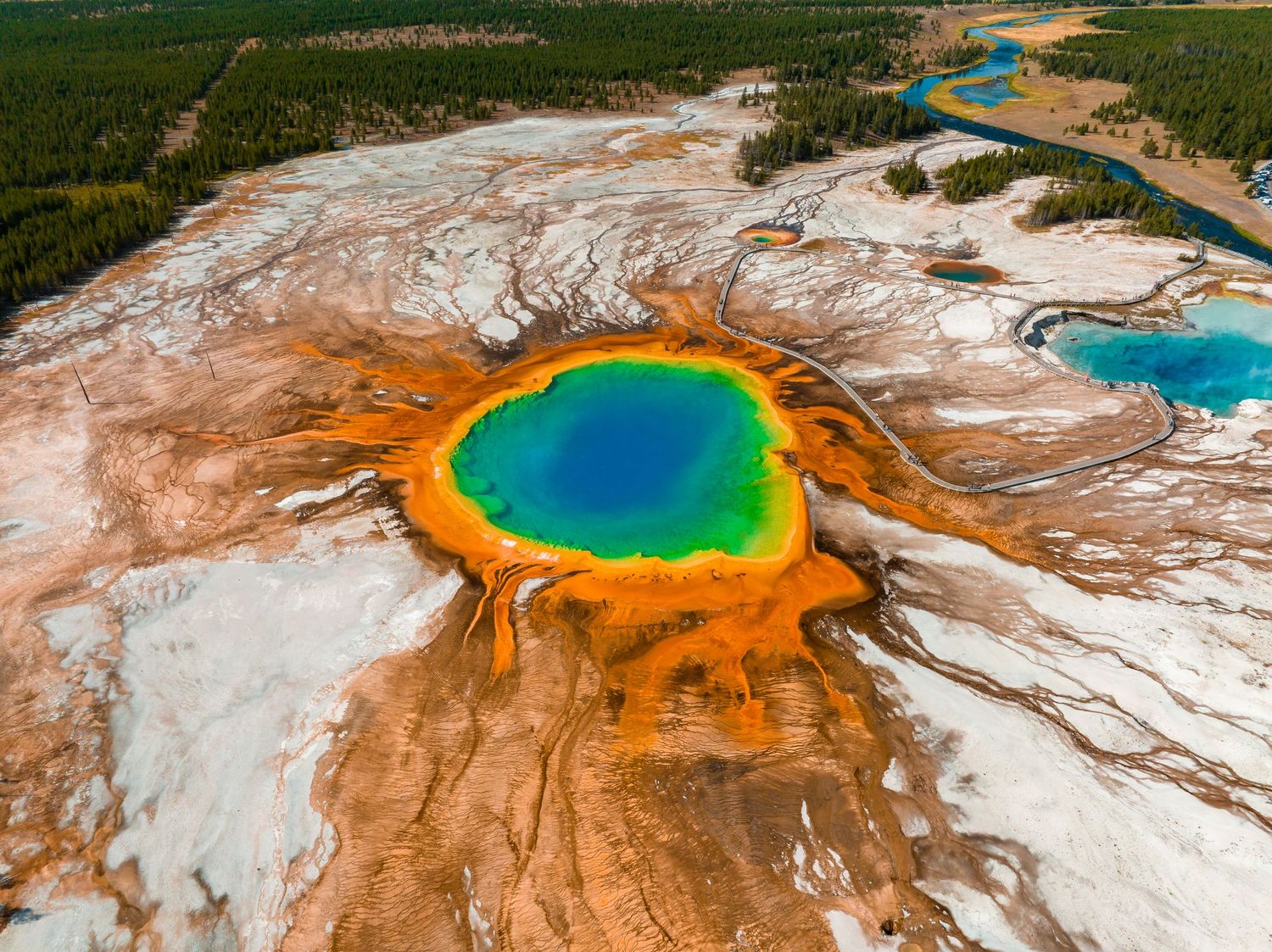 Aerial view of colorful geothermal hot springs with vibrant orange and turquoise pools.