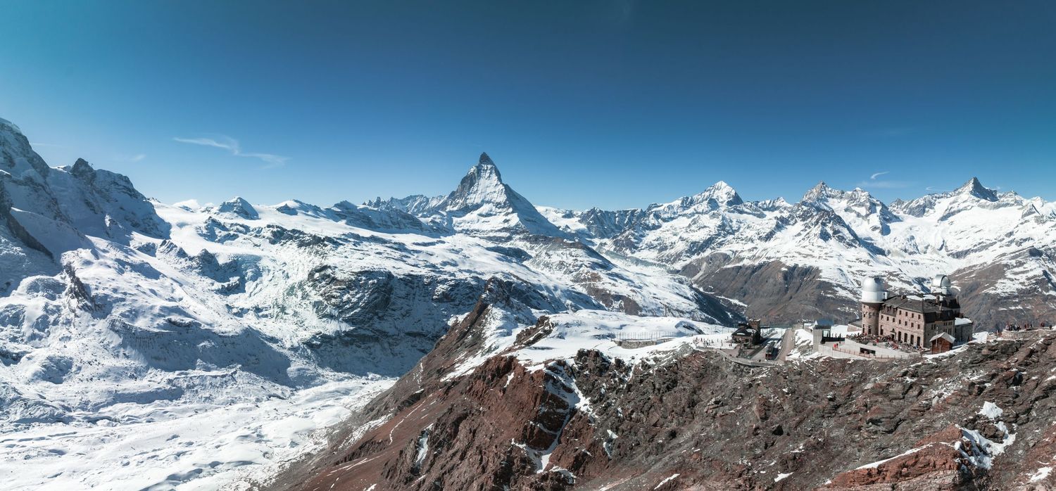 Snow-capped mountain peaks rise dramatically against a clear blue sky in the Swiss Alps.