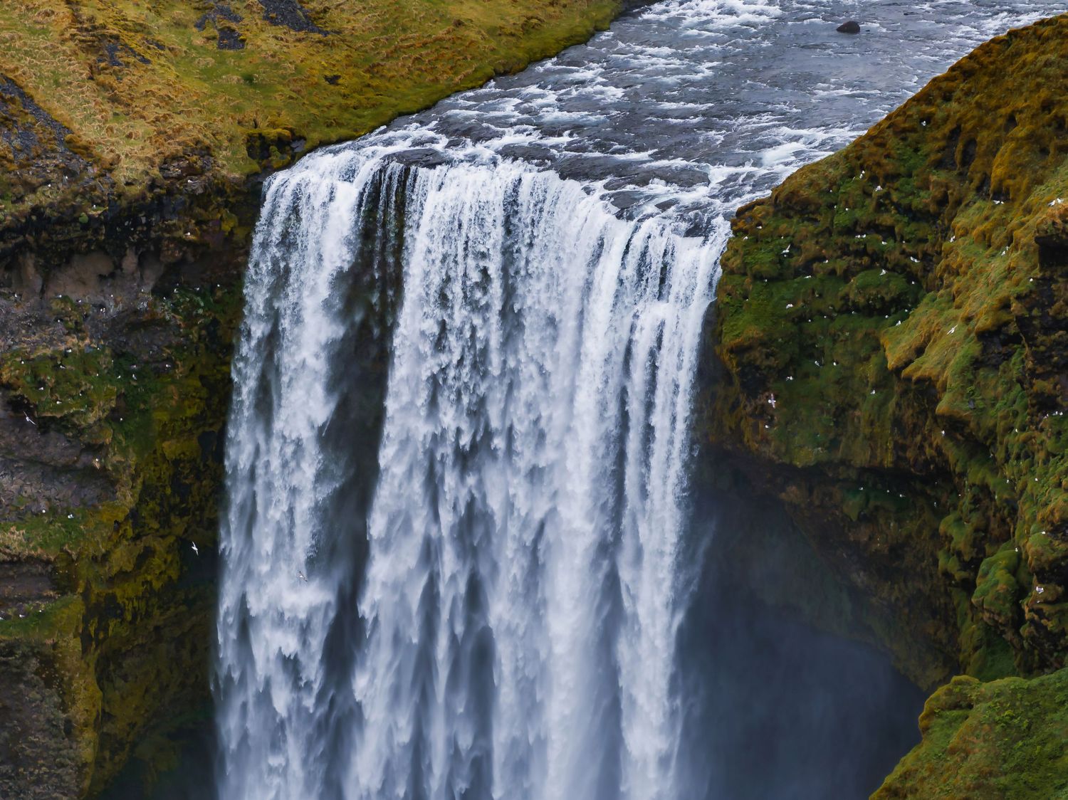 Dramatic waterfall cascades down steep rocky cliffs surrounded by lush vegetation and misty spray.