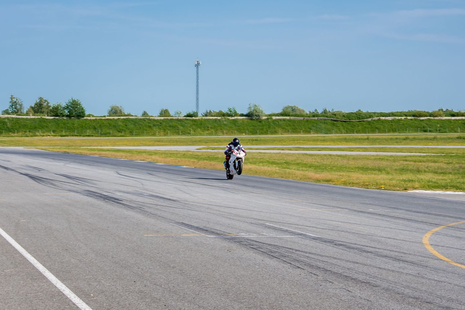 Lone motorcyclist riding on an empty race track with green fields in the background.