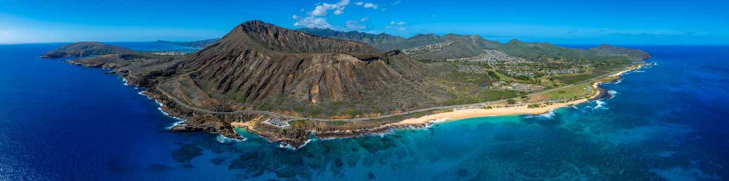 Panoramic coastal landscape with dramatic cliffs and turquoise ocean waters under blue skies.