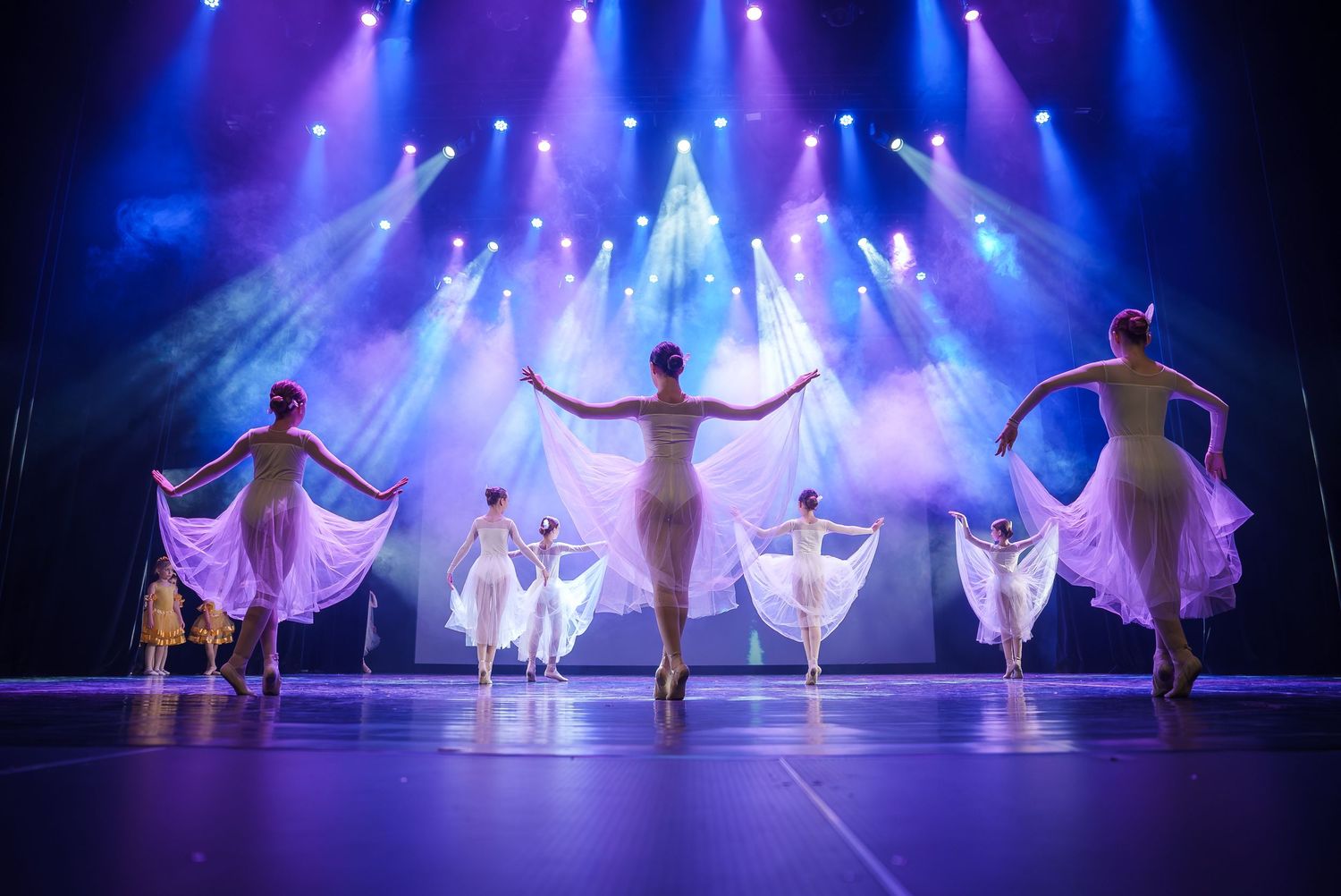 Ballet dancers performing on stage with dramatic blue and purple lighting effects.