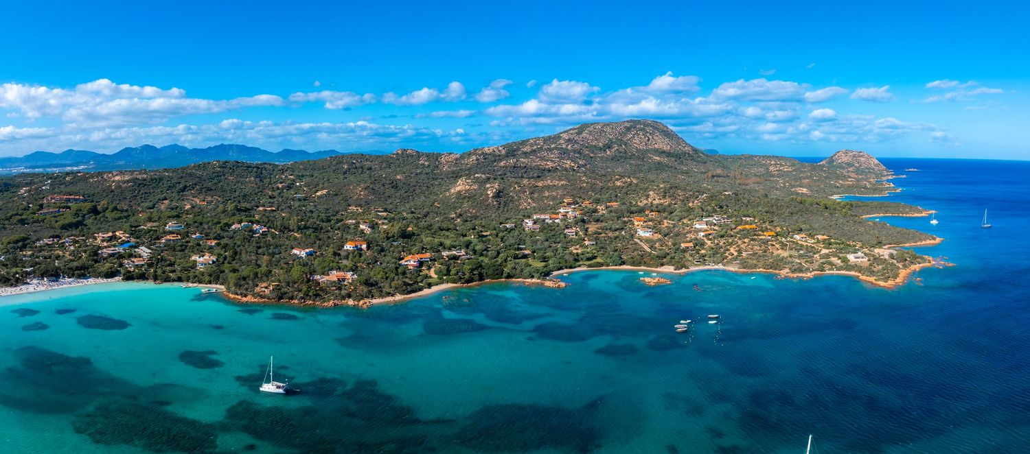 Aerial panorama of tropical coastline with turquoise waters and lush green islands under blue skies.