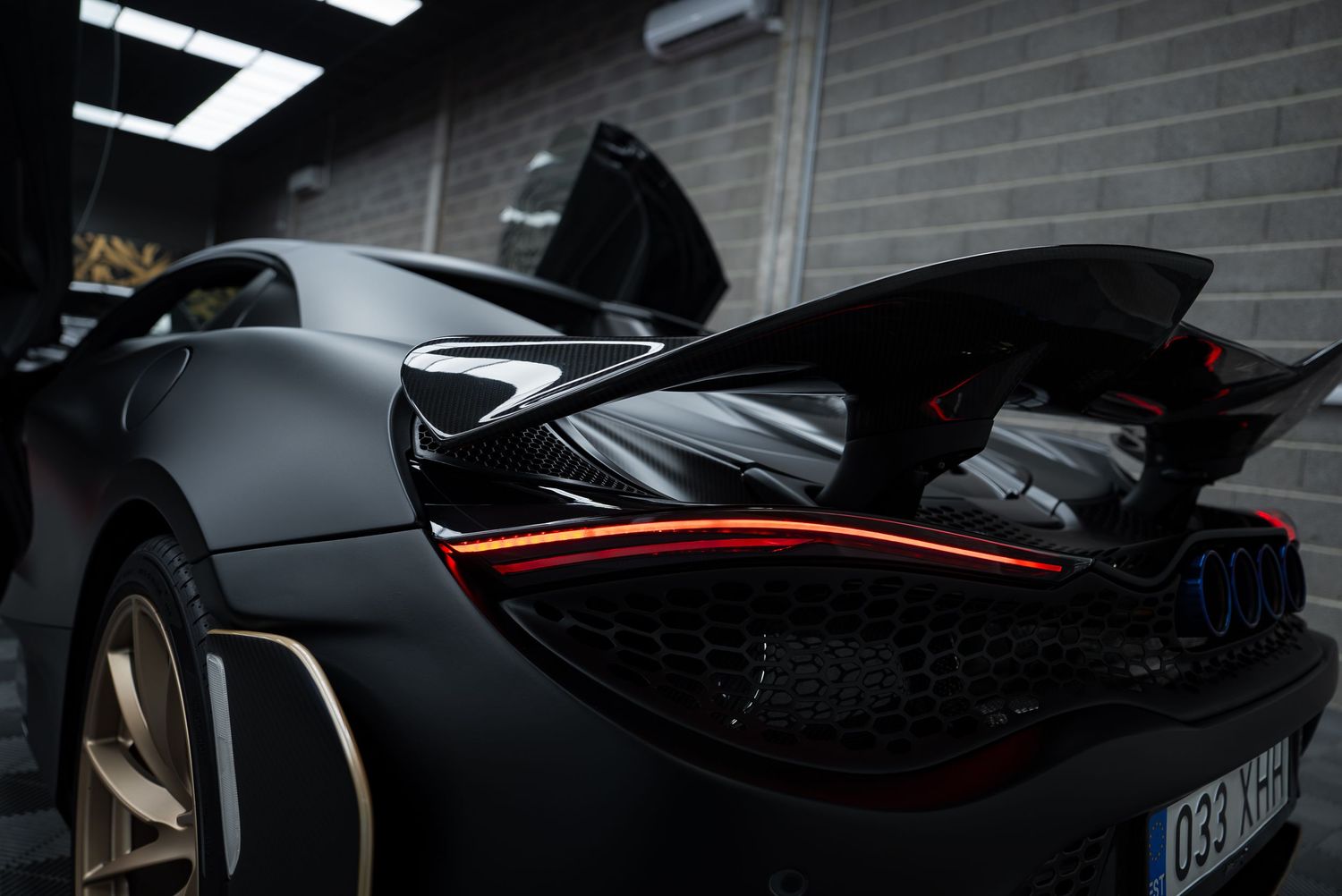 Rear spoiler and taillights of matte black McLaren supercar with red accent line.